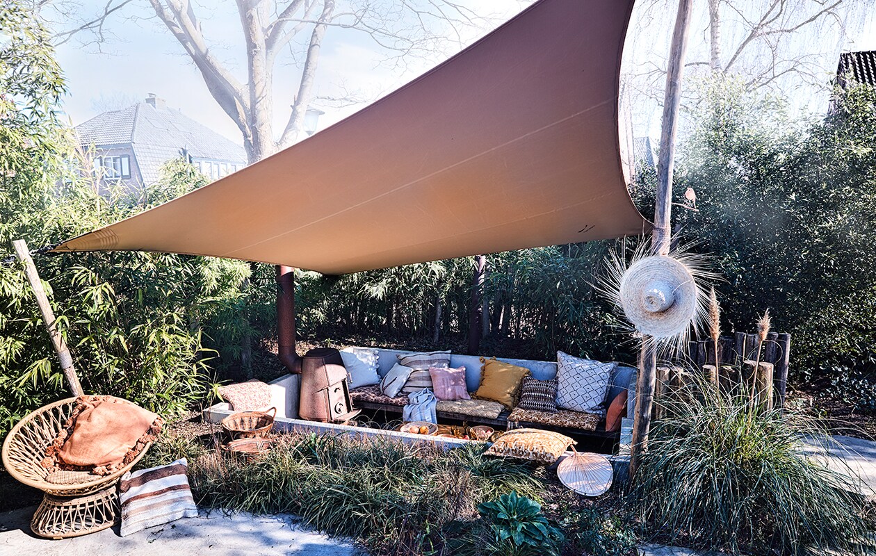 Tent schaduwdoek op maat gemaakt (tentworx.nl). Hoed, gestreept berber kussen 50×50 cm, ecru kelim kussen met pijl 50×50 cm, groot berber kussen met schuine ruit 80×80 cm, groot gestreept kussen 75×75 cm, roze kelim kussen 50×50 cm, decoratief waaier, bamboe salontafel van Tine K Home 70x150x45cm (bxlxh), manden in het gras, naturel linnen handdoek van Libeco (couleurlocale.eu). Gedessineerde matraskussens 60×100 cm, grote kussens met kwasten 65×65 cm, kussen met oranje batik dessin 50×50 cm, kussen met bordeauxrood en oranje dessin 50×50 cm, allemaal Madam Stoltz (deens.nl). Ronde rattan draaistoel Peacock van Arti 89x81x73 cm (lxdxh) (fonteyn.nl).