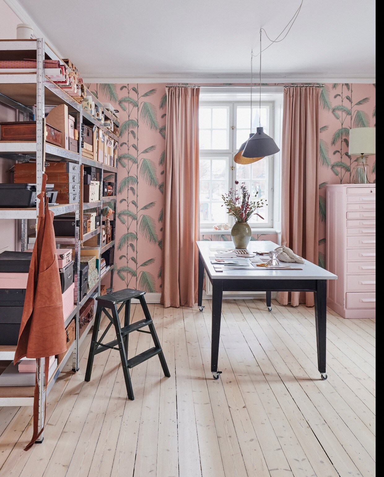 Eva-Marie bekleedde oude lampen van een markt aan de binnenkant met bladgoud en schilderde de buitenkant in kleur 5503 van Flügger. In de oude stalen kasten zijn materialen opgeslagen in mooie dozen en mappen. Bloemen van keeps.dk, kunst op tafel van Kirsten Brandt. Behang Cole &amp; Son. Muurverf 2411 van Flügger. Gordijnen gemaakt van stof van Au Maison. Behang Cole &amp; Son. Gordijnen gemaakt van stof van Au Maison, rail Jotex. Archiefkast geschilderd in kleur 2411 van Flügger.