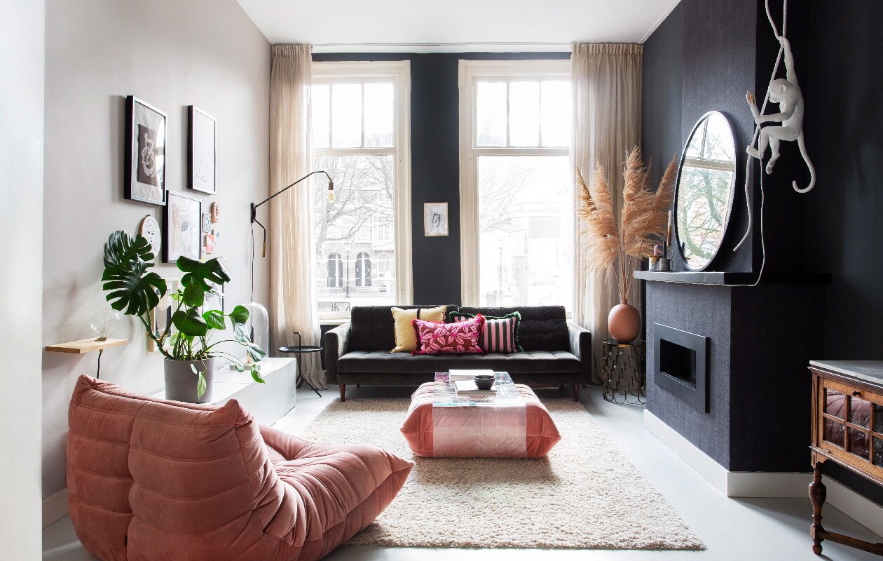 Fauteuil Togo via Fritzvintage, bank Loods 5, tafel en spiegel Fonq. Dressoir, pot en plant Ikea. Vloerkleed en donkere verf IG KH M -111 Karwei. Wandlamp en gouden tafeltje Yaya. Kussens Palais, lamp Monkey van Seletti. Vitrinekastje erfstuk. Vaas met pampasgras Noa May, zwart tafeltje Hay. Lampplank Frama.