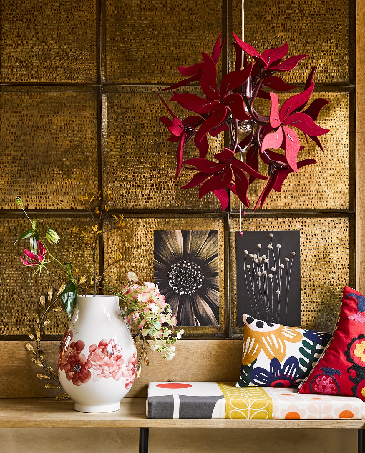 Vaas met rode bloem (polspotten.nl). Gebloemd kussen Sommaraster, 30×60 cm (lxb), hanglamp Ramsele, Ø 43 cm (ikea.nl). Koperkleurige krans, rood gebloemd kussen (brechtjeolsthoorn.nl). Hoes zitkussen gemaakt van stof Orla Kiely (eijffinger.com). Sepia abeeldingen en wand van koperkleurige dienbladen privé.