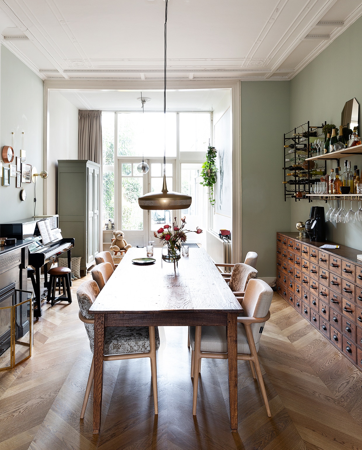 Merijn, Stan en Jonah zitten het liefst aan de lange tafel. Ze kregen hem van Merijns ouders. Stoelen Moooi. Hanglamp Umage. Vaas Sissy-Boy. De lichtgroene kast komt uit het huis van Merijns ouders in Frankrijk; Stan en Merijn verfden hem in de kleur Pigeon van Farrow &amp; Ball. Pianokruk Goossens. Kussen Zuiver. Klok Karlsson. Wandlamp Frama. Fotolijsten met kettinkjes Umbra. Plantenhangers Wehkamp.