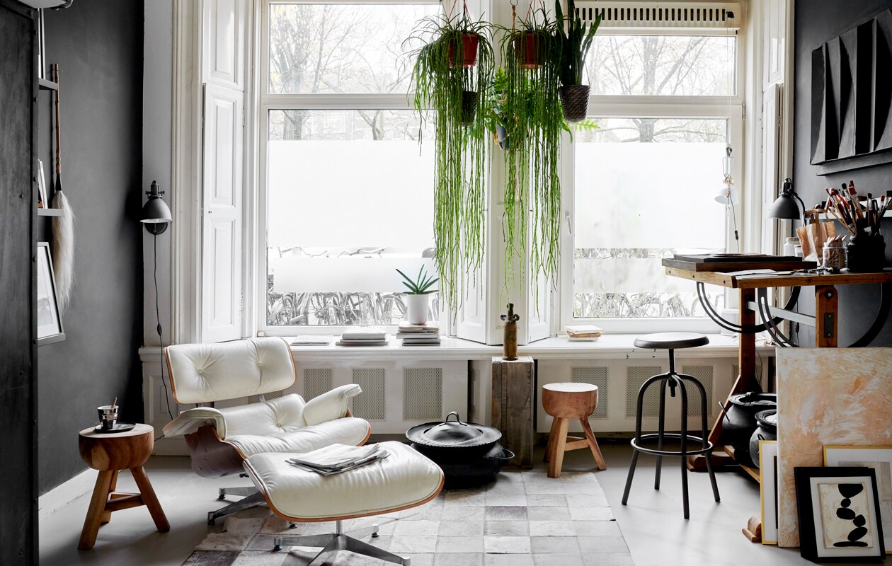 Het atelier in de voorkamer met lounge chair en Ottoman van Eames voor Vitra. Tekentafel, krukken en slagersrek Marktplaats. Lamp Serge Mouille. Leren karpet overgenomen van een vriend. Mand uit Marokko. Sokkel van een markt, de vaas erop is een reissouvenir.