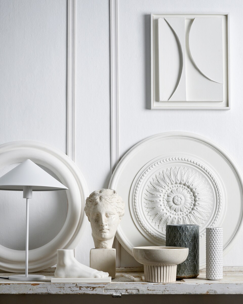 Latten decorlijst mdf, lengte 260 cm per stuk vanaf € 5,50 (karwei.nl). Schilderij, prijs op aanvraag (artinreturn.nl). Ornament PU Rozet 76×76 cm vanaf € 85,-, ornament ring 72x72cm vanaf € 70,-, sculptuur Venus vanaf € 60,- (het-schippertje.nl). Sculptuur voet € 59,95, witte metalen lamp Triangle, 58×40 cm (hxØ) € 119,- (hkliving.nl). Kom Indi met spikkelglazuur, 26×16 cm (hxØ) € 35,- (made.com). Vaas Bubble van Bloomingville € 21,-, vaas Mystic print van Serax, 25,5×17 cm (hxØ) € 22,- (vtwonen.nl).