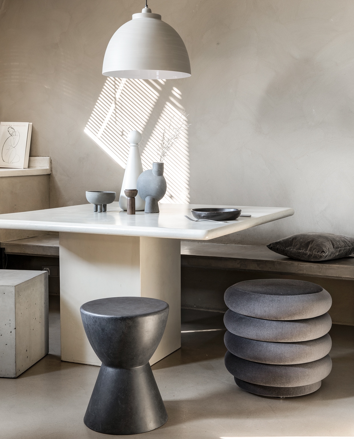 Eettafel van de kringloopwinkel, in beton-ciré gezet, prijs op aanvraag (betoncirenederland.nl). Vierkante kruk van beton (debetonfabriek.nl). Kruk van fiberclay, antracietgrijs, ook voor buiten (woood.nl). Poef fluweel (fermliving.com). Vaasje Sphere mini, vaasje Sphere medium (casagitane.com). Witte fles met dop Muses Era, zoutmolen Drupe mill, in smoked ash (fermliving.com). Hanglamp in betonlook (karwei.nl). Bord Black Pottery (couleurlocale.eu). Kussen bruin fluweel, 45×45 cm (loods5.nl). Bestek privébezit.