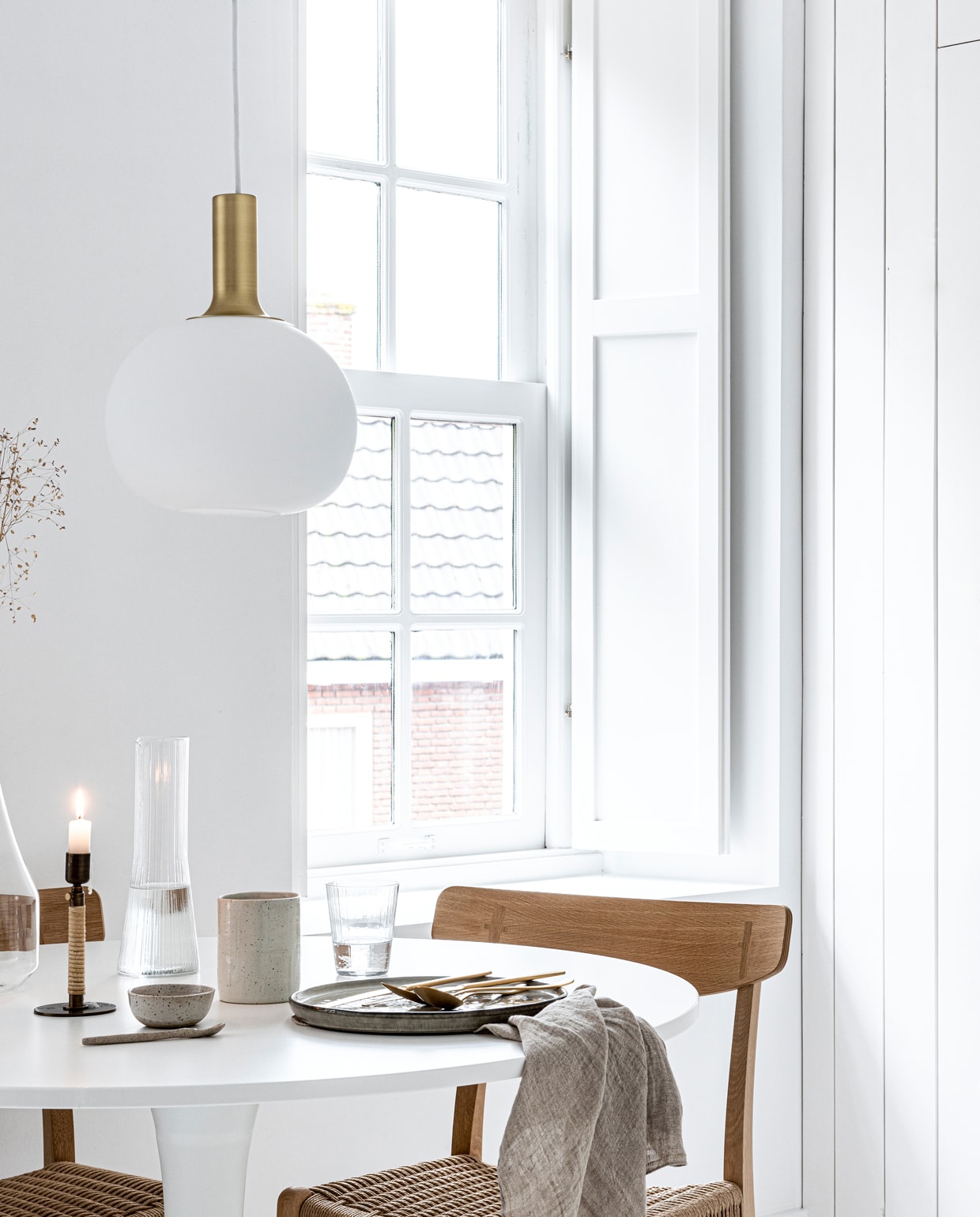 Hanglamp Alton 25 van Nordlux, groen dinerbord uit de Artisan collectie van Salt &amp; Pepper, Ø 26,5 cm, gouden bestek van Amefa, theedoek uit de vtwonen collectie, 60×60 cm (vtwonen.nl). Witte ronde eettafel Docksta (ikea.nl). Eikenhouten eetkamerstoel met gevlochten zitting CH23 van Carl Hansen &amp; Søn (coosdewitwonen.nl). Messing kandelaar omwikkeld met rotan Duca (menu.as). Glazen karaf met handvat, drinkglas met ribbels, kegelvormige glazen kan met ribbels, beker aardewerk (zarahome.com). Overig privébezit.
