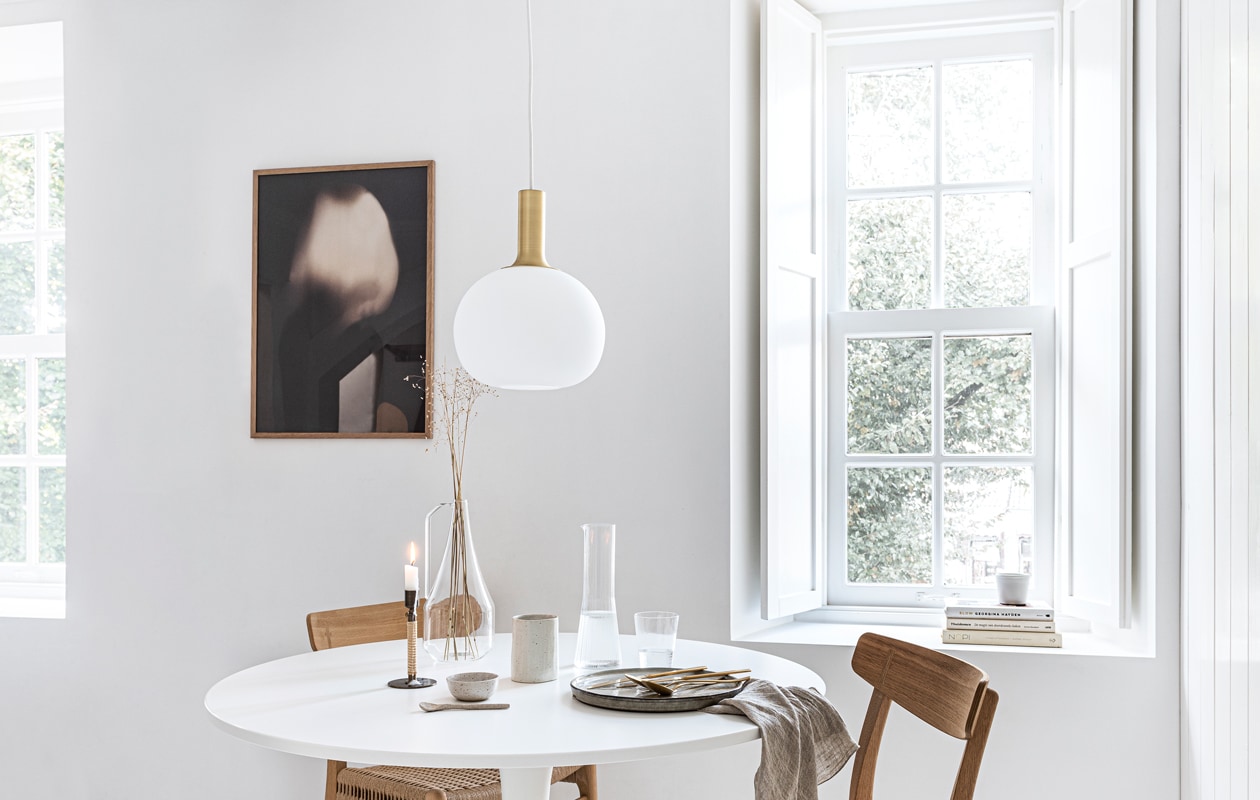 Art print van Gurilla, 50×70 cm, eikenhouten frame, 50×70 cm (theposterclub.com). Hanglamp Alton 25 van Nordlux, groen dinerbord uit de Artisan collectie van Salt &amp; Pepper, Ø 26,5 cm, gouden bestek van Amefa, theedoek uit de vtwonen collectie, 60×60 cm (vtwonen.nl). Witte ronde eettafel Docksta (ikea.nl). Eikenhouten eetkamerstoel met gevlochten zitting CH23 van Carl Hansen &amp; Søn (coosdewitwonen.nl). Messing kandelaar omwikkeld met rotan Duca (menu.as). Glazen karaf met handvat, drinkglas met ribbels, kegelvormige glazen kan met ribbels, beker aardewerk (zarahome.com). Overig privébezit.