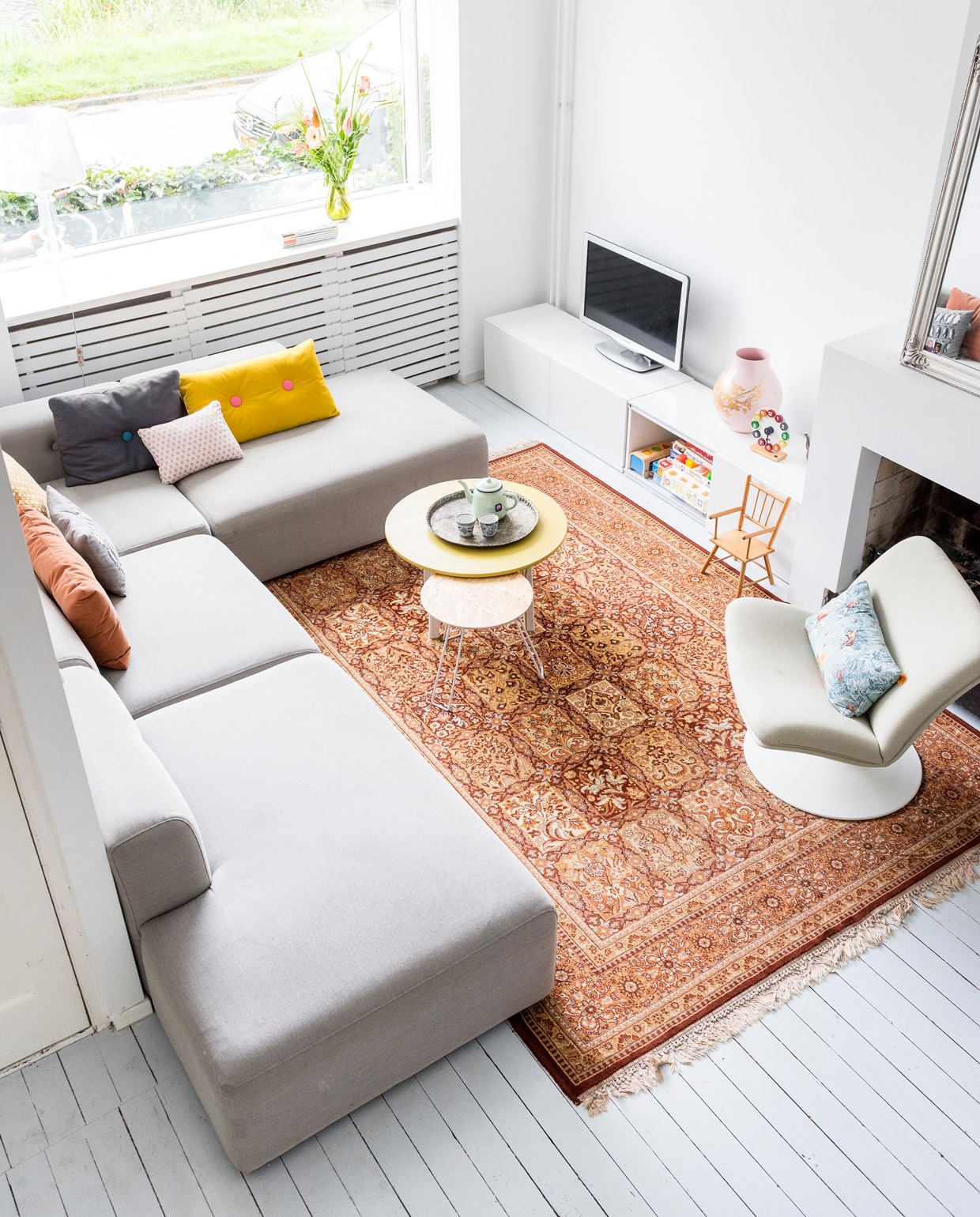 Bank van Hay via Depot Rotterdam, vloerkleed van martkplaats.nl, klein kussen van Hay, andere kussens van ByAlex, vaas van Hella Jongerius voor Ikea, tv-meubel Besta van Ikea, spiegel Xenos, klokje en kinderstoel vintage, rond tafeltje van Zuiver. ‘De grotere ronde vintage tafel is geverfd en ingekort. De Artifort-faurteuil is een erfstuk van mijn oma, die heel hip was.’