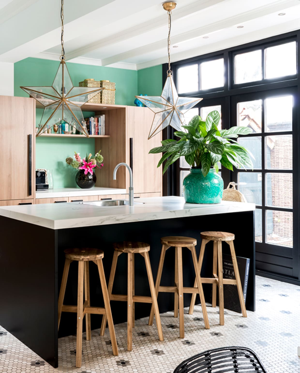 Keuken van Piet Boon. Stervormige lamp van Sissy-Boy. Plantenpot Mica Decorations. Vloertegels van designtegels.nl. Krukjes Ikea. Ananas links op het aanrecht komt uit Parijs, evenals de windlichten boven op de keukenkast, verkrijgbaar bij Studio Sophie. Muurverf kleur Arsenic van Farrow &amp; Ball.