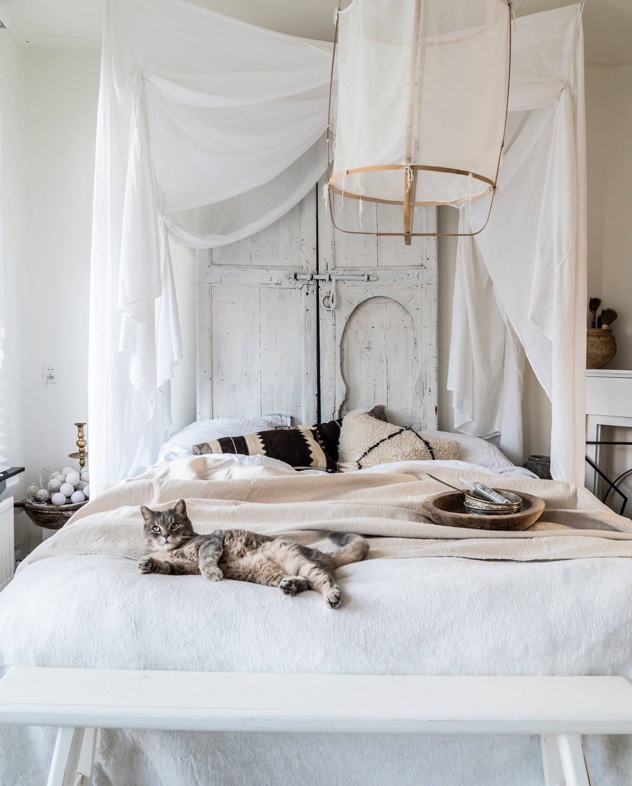 Pompon-deken van noamay.nl, beddengoed van H&amp;M Home, kussens op bed van noamay.nl en meegenomen uit Marrakech, linnen klamboe van Numero 74 via lidor.nl, houten pot van Simply Pure Home, houten schaal op bed overgenomen van een styliste, raambekleding van Inside Blinds, vloerkleed uit Marrakech.