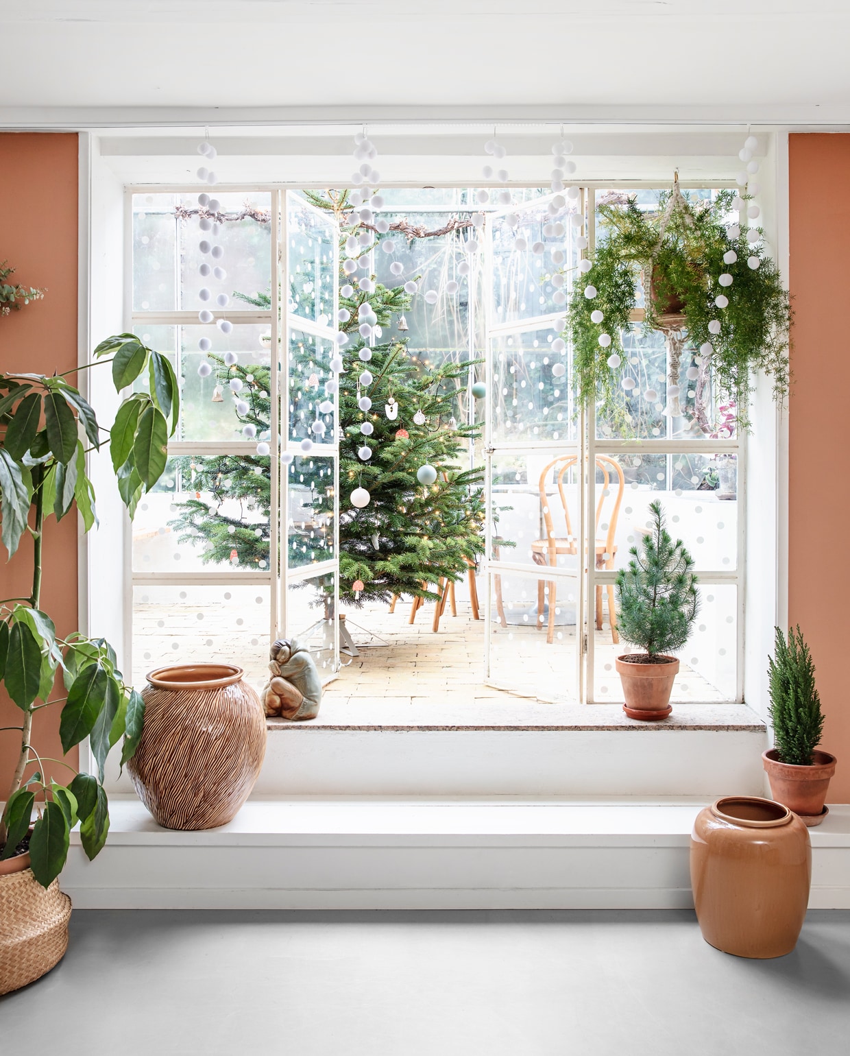 De keuken en eetkamer bevinden zich in het souterrain van het huis en geven toegang tot de serre waar het gezin het hele jaar door te vinden is. De overgang tussen het eetgedeelte en de orangerie is weelderig gedecoreerd met groene planten (hellonature.dk). Op de muur kleur Terra di Siena van Flügger. Op de glazen deuren heeft Rikke een decoratie van sneeuwvlokken aangebracht.