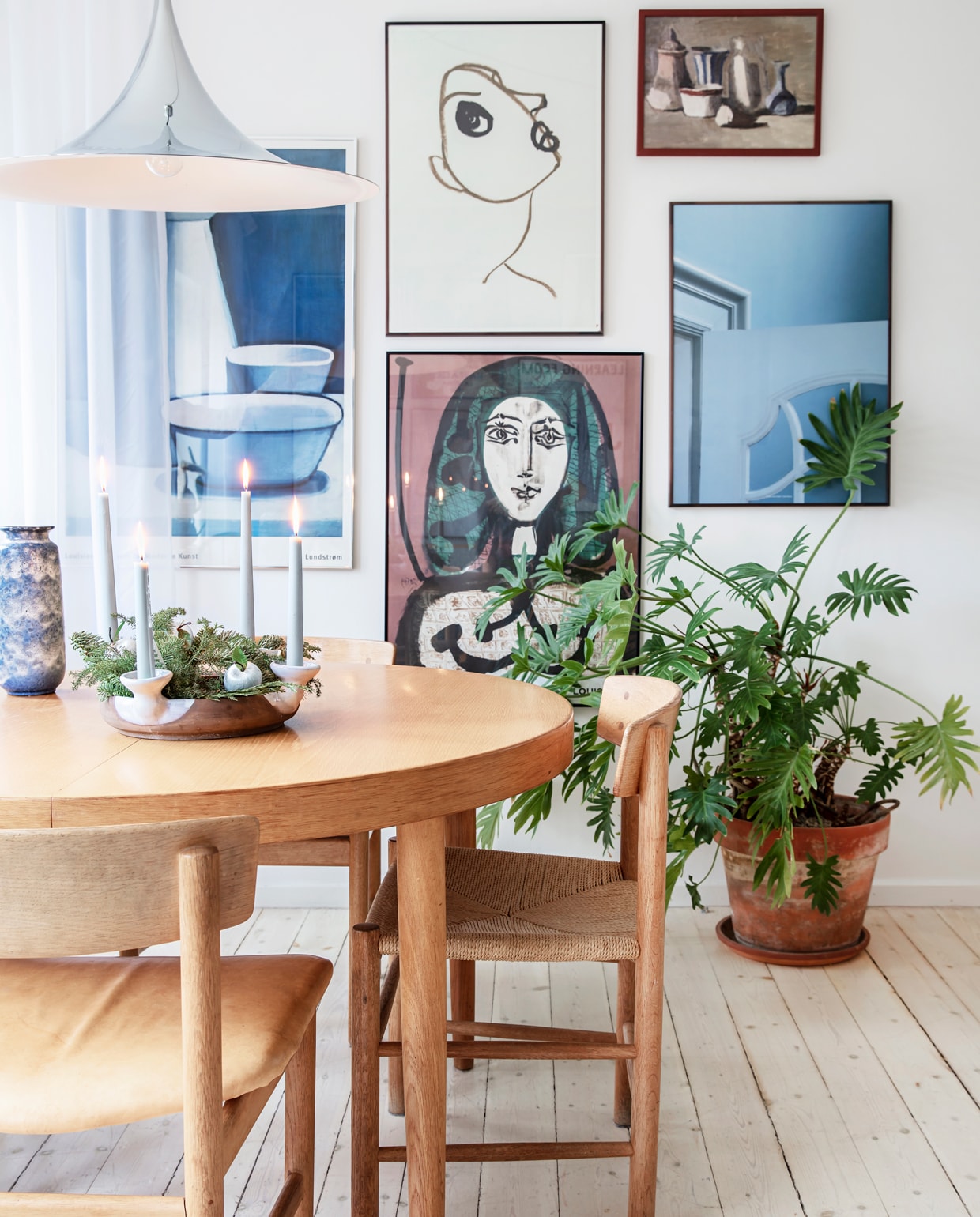 De tafel en stoelen van Børge Mogensen zijn vintage. Lamp van Gubi. Aan de muur posters van tentoonstellingen, een schilderij van een vlooienmarkt en een poster van Kristina Dam. Ook de bustes zijn rommelmarktvondsten. Kerstkrans zelfgemaakt en opgehangen aan een leren band, die past bij de kleuren en materialen van de eetkamer.