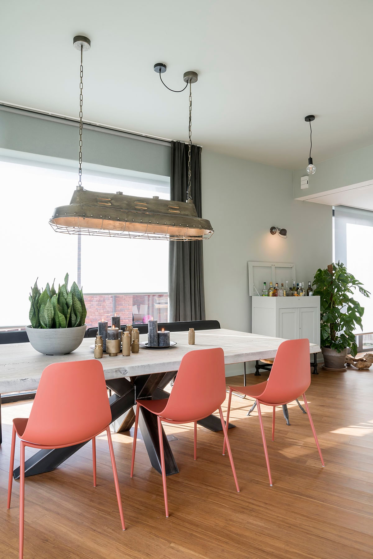 Rolgordijn Howland grijs (). Glasgordijn Velluto Vison (). Wandlamp (Lucide), hanglamp – boven eettafel (BePureHome), eettafel (PMP Furniture), eetkamerstoel (Kave Home). Hanglampen – verspreid, drankenkast (privébezit).