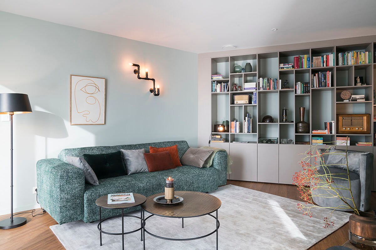 Bibliotheekkast – melamine steengrijs (). Tapijt (Floorline), vloerlamp (Woood), salontafels Elton (Lifestyle), poster (Paper Collective), vloerlamp (Lucide).