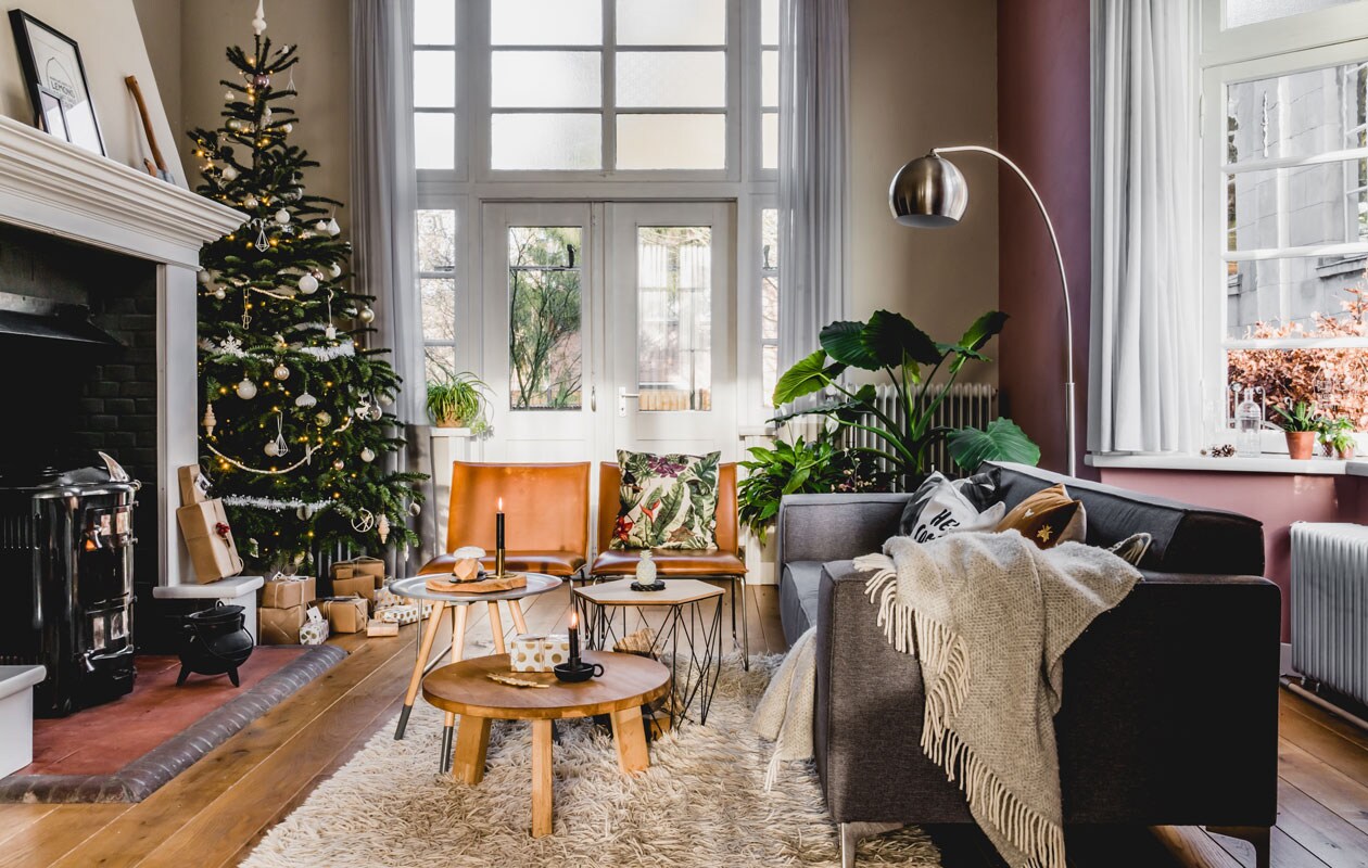 De grote boom staat mooi naast de bakstenen schouw, die met plamuur en verf werd opgefrist. Elk jaar komen er een paar nieuwe versierinkjes bij voor in de boom. Bijzettafels van Xenos en Zuiver, bruine fauteuils van Kwantum, vloerkleed van Ikea.