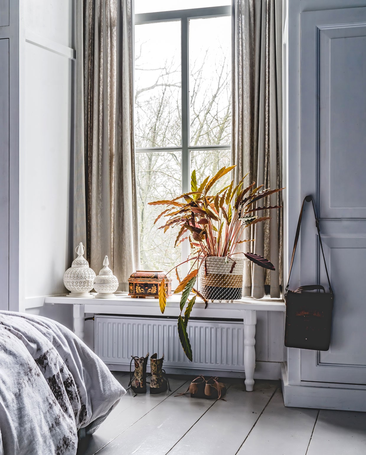 Het tafeltje en de kast maakte de vader van Jankees zelf. De oude, houten vloer werd lichtgrijs geverfd in kleur Balanced Breeze van Flexa. Op het bankje een oude sieradendoos uit Zweden en witte lantaarns die ze al hadden. Plantenmand van Xenos, gordijnen van Hema.