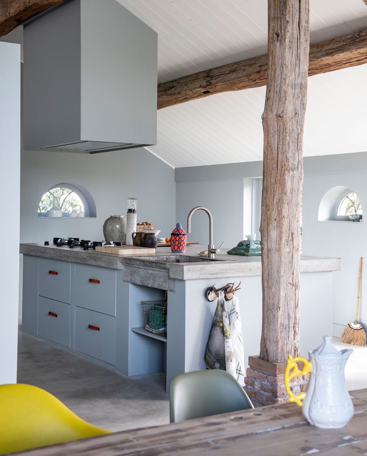 De keuken is geschilderd in de tinten Ash en Mouse van Stapelgoed. Het betonnen blad is ter plekke gestort op een gemetselde constructie. ‘We hechten aan details als de arduinen spoelbak, de geweivormige ophangpunten en de leren ladekastgrepen van Handles and More.’