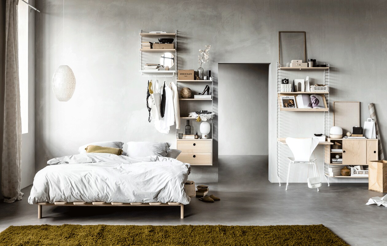 Wandsysteem met witte draadstalen panelen en planken, deuren en werkblad in kleur Ash, (stringfurniture.com). Muurverf kleur North, (bauwerkcolour.com). Vloer Novilon kleur Beton van vtwonen, 200 cm of 400 cm breed, exclusief installeren (vtwonen.be/vtwonen-collectie). Gordijn Dazer van Kinnasand, 320 cm hoog, witte houten vlinderstoel ronde houten opberger met deksel (coosdewitwonen.nl). Parelmoeren hanglamp, ronde spiegel op eikenhouten poot, canvas tas, bruin flesje olie, eikenhouten lijst, doosjes met knoopjessluiting, plastic kratten, witte kartonnen opbergers, zachtgrijze leren tas met bruin leren koord (letoile.store). Massief beukenhouten bed Modest (loof.nl). Dekbedovertrek met bijpassende slopen van percal katoen in kleur Misty Grey (yumeko.nl). Sierkussen, raffia instappers (zarahome.com). Okergeel berbertapijt, verkrijgbaar in elke maat en kleur, 220×340 cm (lxb) (paullelieveld.com). Zwarte ovale marmeren schaal op poten van Ferm Living, grijze glazen karaf van Ferm Living, tafellamp met grijze betonnen poot van Menu, tafellamp met gebroken wit onderstel van Menu (vtwonen.be). Zwart houten object in cilindervorm zwart houten object in puntvorm, zwart houten opbergschaaltje (loods5.nl). Metalen brillenkoker, grijze fluwelen toilettas met gele kwast (maisonnl.com). Overig privébezit.