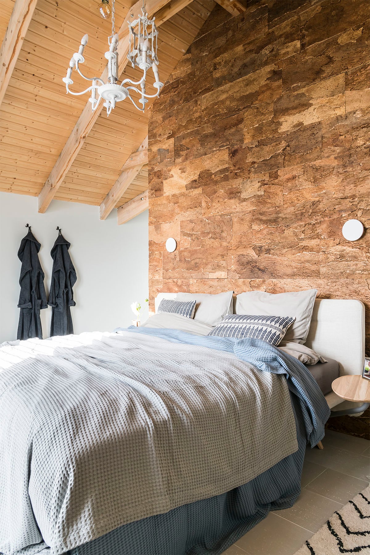 Kurkwand – Maximo uit Raw collectie (). Wandlamp (Lucide), bed – Fly (Velda), badjas (Walra), dekbed (vtwonen collectie), blauwe sprei (Heckett &amp; Lane), grijze sprei (Vandyck), kussen op bed (HKliving), tapijt (HKliving).