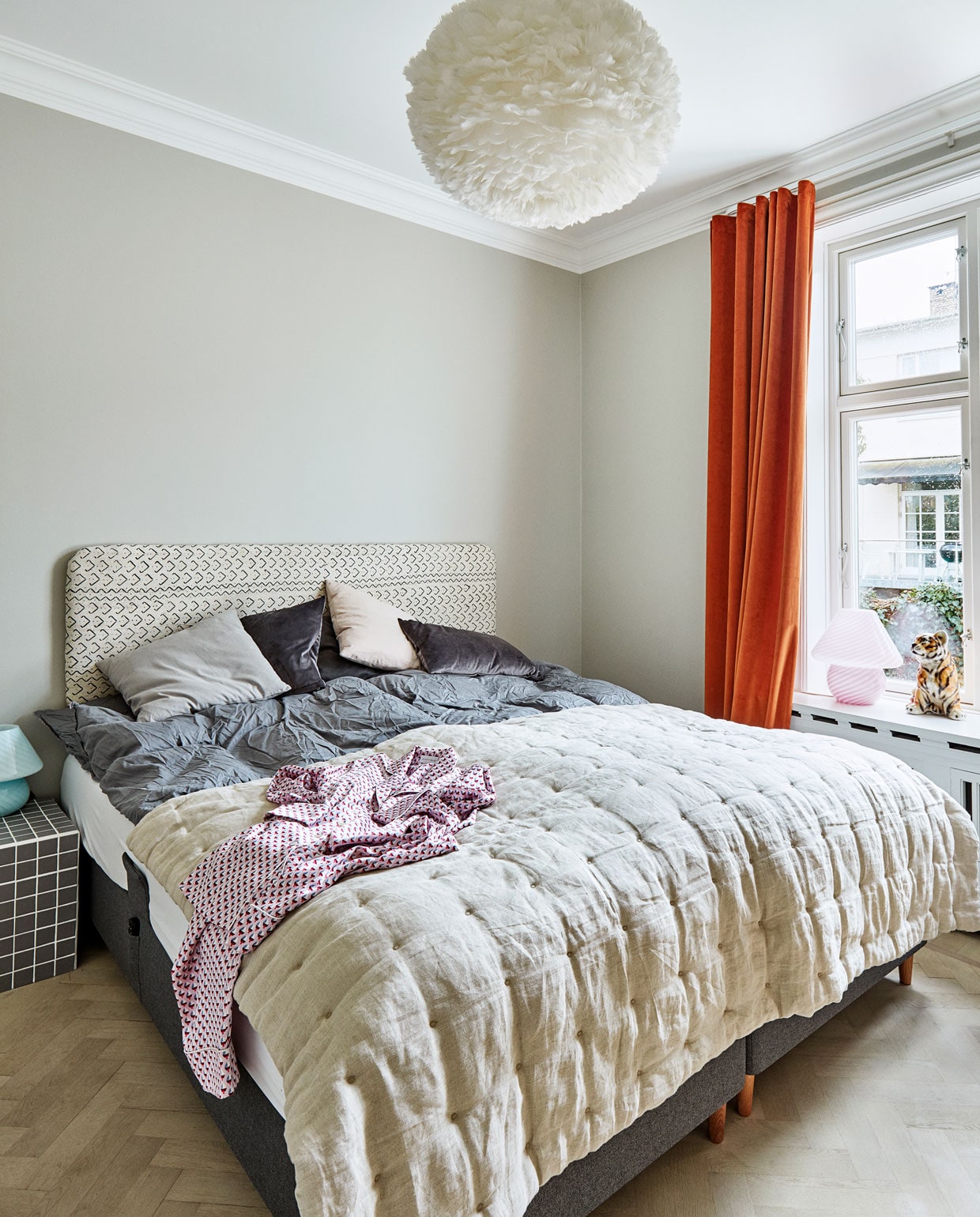 De doorgestikte plaid en kussens zijn van &amp;Drape, net als alle gordijnen in huis. Het bedhoofd en nachttafeltje zijn zelfgemaakt. Hanglamp van Vitra.