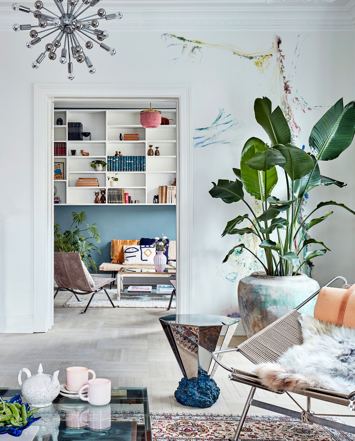 Kijkje vanuit de zithoek richting de bibliotheek met zijn originele open wandkast. Op de voorgrond de Flagline Chair van Hans Wegner, de Diamant Table van Fos, lamp Sputnik van Paul de Haan en een vintage salontafel van Belgo Chrom. Op de achtergrond stoel PK 22 van Poul Kjaerholm, een vintage salontafel van Romeo Rega en een daybed van Ikea. De muur rechts is beschilderd door kunstenaar Jacob Steen.