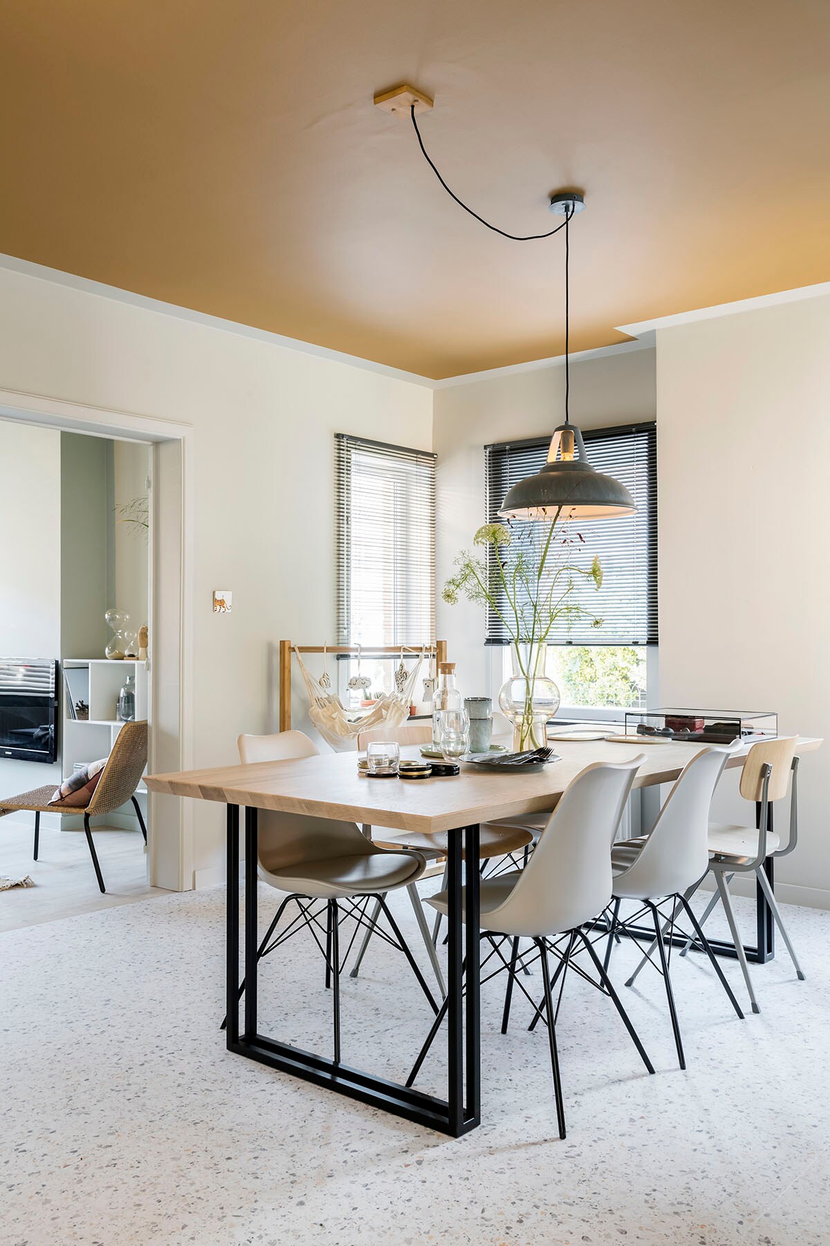 Kleur op de muur en boord plafond: G0.05.70 (). Kleur op plafond: E4.30.50 (). Hanglamp (Lucide), eettafel (Vincent Sheppard), stoel – wit (Tenzo), stoel – hout (Hay), baby hangmat en standaard (La Siesta).