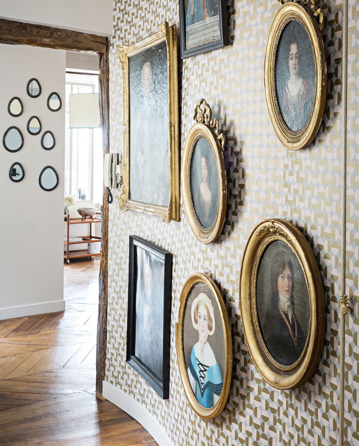 Aan de ronde muur in de gang met behang van Au fil des Couleurs hangen negentiende-eeuwse olieverfportretten in mooie lijsten die het stel door de jaren heen heeft verzameld.