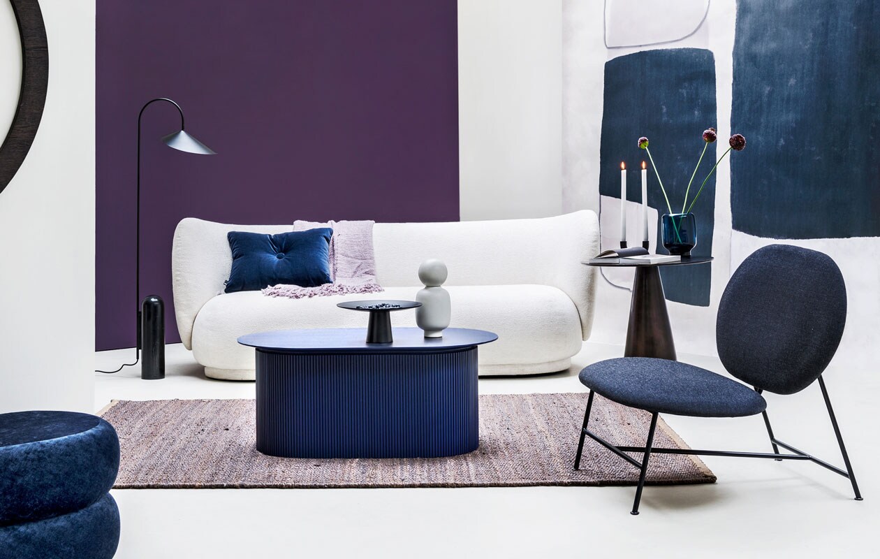 Paarse muurverf Moorland van vtwonen, (karwei.nl). Behang uit collectie Wallpower, 3×3 m (eijffinger.com). Bank Rico 3 met bouclé bekleding, 210×78,5×79 cm (lxbxh), blauwe salontafel, ovale poef van blauw fluweel, lamp met stenen voet (fermliving.com). Zetel van Northern, 80x78x73 cm (lxbxh) (goeds.nl). Metalen tafeltje, 60×56 cm (bxh) (hkliving.nl). Hennep tapijt 101 Copenhagen, 160×230 cm (casagitane.com). Lila plaid (malagoon.com). Schaal op voet van Broste, object/vaas Talia en kandelaar Arch beide van Ferm Living, fluwelen kussen van Hay, glazen vaas van Menu (vtwonen.be).