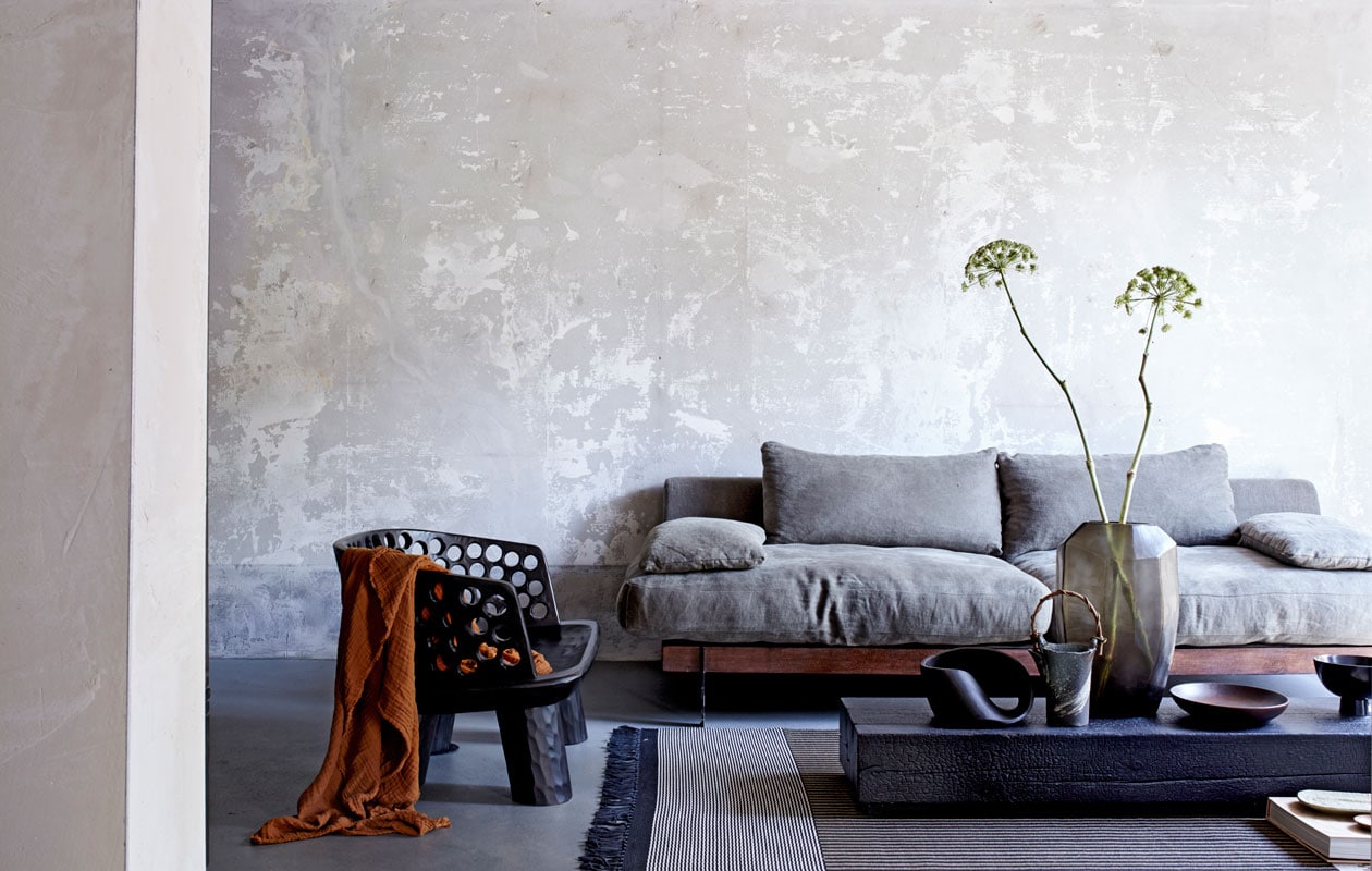 Zwarte houten fauteuil, zwart object op salontafel (badenbaden.nl). Zeter Ciel met linnen bekleding van l’Authentique, 220x100x70 cm (bxdxh) (deruverfenbehang.nl). Vloerkleed grotendeels gemaakt van papier, 240×170 cm (lxb) (vloerkledenwinkel.nl). Roestkleurige plaid, zwarte kom op voet (hm.com). Salontafel van zwart gebrand hout, glazen vaas (covanderhorst.nl). Keramieken kan met bamboe handvat (japansewinkeltje.nl). Ovaal zandkleurig keramieken bord (desimonewayland.com). Houten schotel (restored.nl). Overig privébezit.