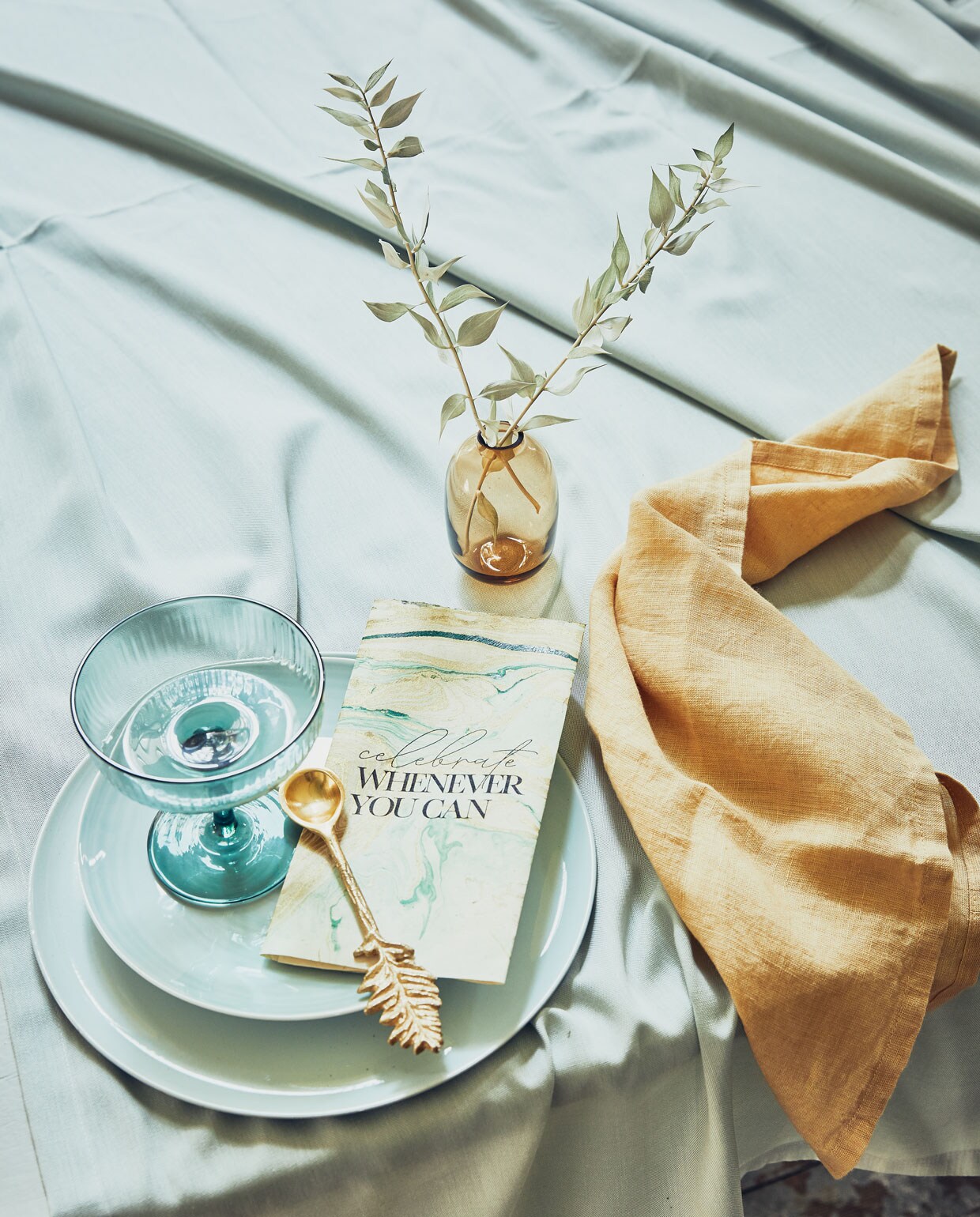 Marmerpapier (vanbeekonline.com). Champagnecoupe, minivaasje, lepel uit set van 3, blauw tafelkleed (hm.com). Okergeel linnen servet (hkliving.nl). Dinerborden, mintgroene borden, Ø 20,7 cm (vtwonen.be).