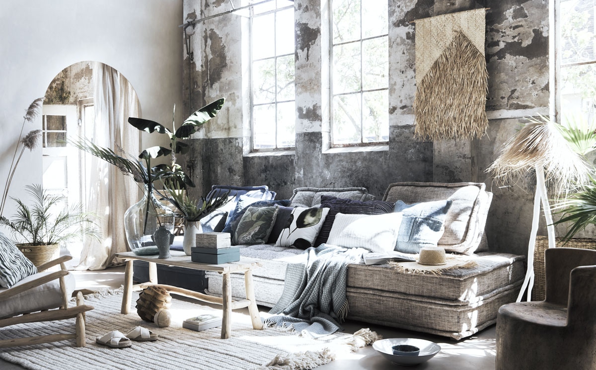 Bamboe mand met handvat van Rivièra Maison, Novilon vloer Zand (vtwonen.be). Muurverf Ibiza op de muur met boog (bauwerk.com.au). Stoel met witte kussens (householdhardware.nl). Bank (rivieramaison.nl). Bruine stoel, gevlochten rieten wandkleed (couleurlocale.eu). Donkerblauw kussen van Aai made with love, kussen met print blauw en groen, wit kussen met bladmotief, houten tafel, gestreept kussen in stoel (loods5.nl). Blauw kussen met dierenprint (couleurlocale.eu). Donkerblauw kussen met streep, wit kussen met smalle streep (letoile.store). Lichtblauw kussen (couleurlocale.eu). Kant-en-klare linnen gordijnen (bymolle.com). Vloerkleed van Tibetaanse wol, boek, witte schaal (sukha.nl). Blauwe plaid, lamp met witte houten voet en raffia kap (letoile.store). Houten sierbol, stenen sierbol, blauwe houten dozen, rieten hoed, vaas met vlechtwerk langs bovenkant (zarahome.com). Vaas in visvorm (maisonnl.com). Witte slippers, blauwe kom (hm.com). Mand rechts achterin (com-anders.nl). Groendecoratie (judithslagter.nl). Grote glazen vaas (vandijkenko.nl).