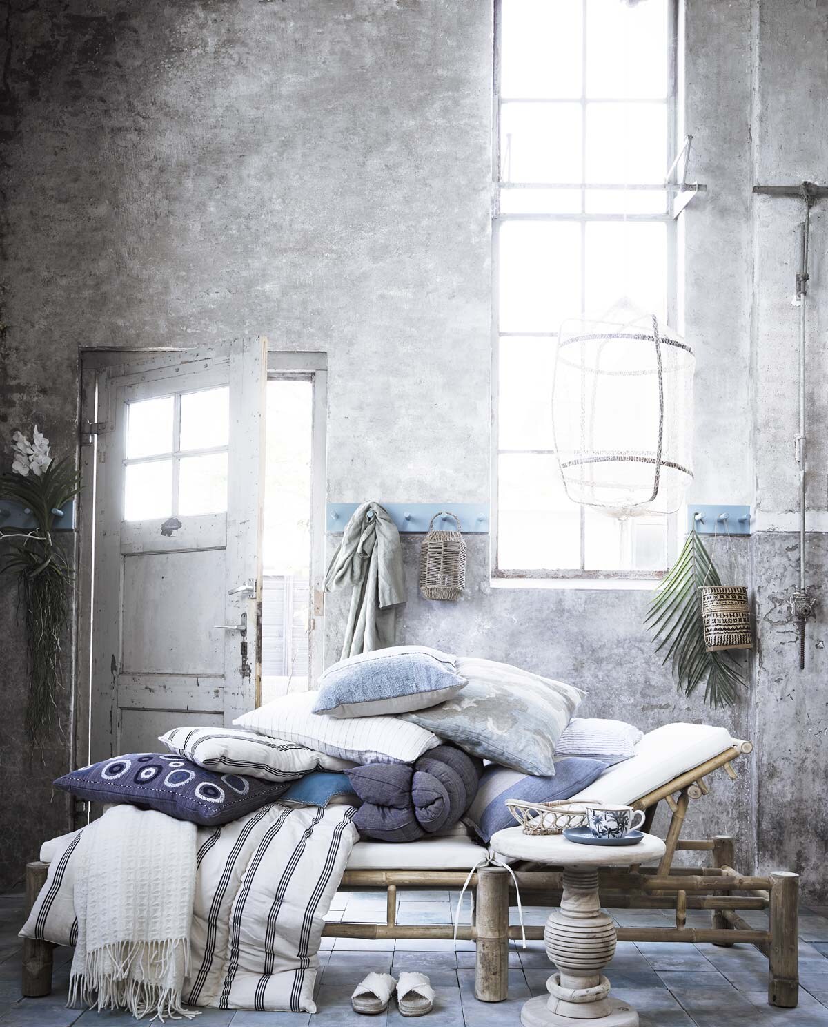 Blauwe tegels (oudebouwmaterialen.nl). Daybed van Tine K Home (wehkamp.nl). Blauwe kapstok (com-anders.nl). Groendecoratie (judithslagter.nl). Bruine lantaarn van zeegras, gevlochten mandje, mok met print, witte slippers, groene linnen badjas (hm.com). Bruin tasje (loods5.nl). Blauw bordje maat S, hanglamp, witte plaid, opgerold donkerblauw kussen, witte plaid met blauwe streep, wit en blauw kussen met smalle streep (letoile.store). Blank houten tafeltje (zarahome.com). Kussen met ronde vormen, blauw kussen met luchtdessin van John Derian, blauw kussen met brede bruine streep (wva.nl).