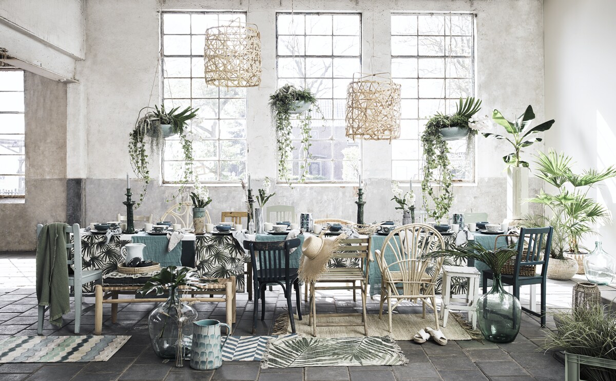 Witte tafel, lichtgroene klapstoel, kan op voorgrond, blauw-bruine vaas op tafel, lichtblauwe kan op bankje, hoge vaas rechts achter (com-anders.nl). Blank houten bankje met geweven leren zitting, blank wilgenhouten stoel Essaouira met gebogen rug, kaarsenstandaards (householdhardware.nl). Blauwe, groene en blank houten stoelen, glazen vazen, witte houten kruk (vandijkenko.nl). Blank houten hanglampen, beige rieten vloerkleed, blauwe kaarsen (letoile.store). Rieten stoel achter de tafel, vloerkleden met print, kunsttakken, blauw-groen-witte kan van Serax, groene krat, schaaltjes met bloemdessin, rieten flessenmand, blauw-witte vaasjes van Serax op tafel, vierkant groen kussen op bankje (loods5.nl). Blauwe linnen stof als tafelloper (wva.nl). Tafellopers met palmprint, blauwe kommen, blauwe borden, groene plaid, rond rotan dienblad, witte mokken, groene lepels, witte slippers, lantaarn van zeegras, lichtblauw gewassen linnen servetten, ronde blauwe pot met deksel (hm.com). Hangplanten met schalen en overige groendecoratie (judithslagter.nl). Rieten hoed, mand met witte driehoeken (zarahome.com). Beige linnen servetten (bymolle.com). Overig privébezit.
