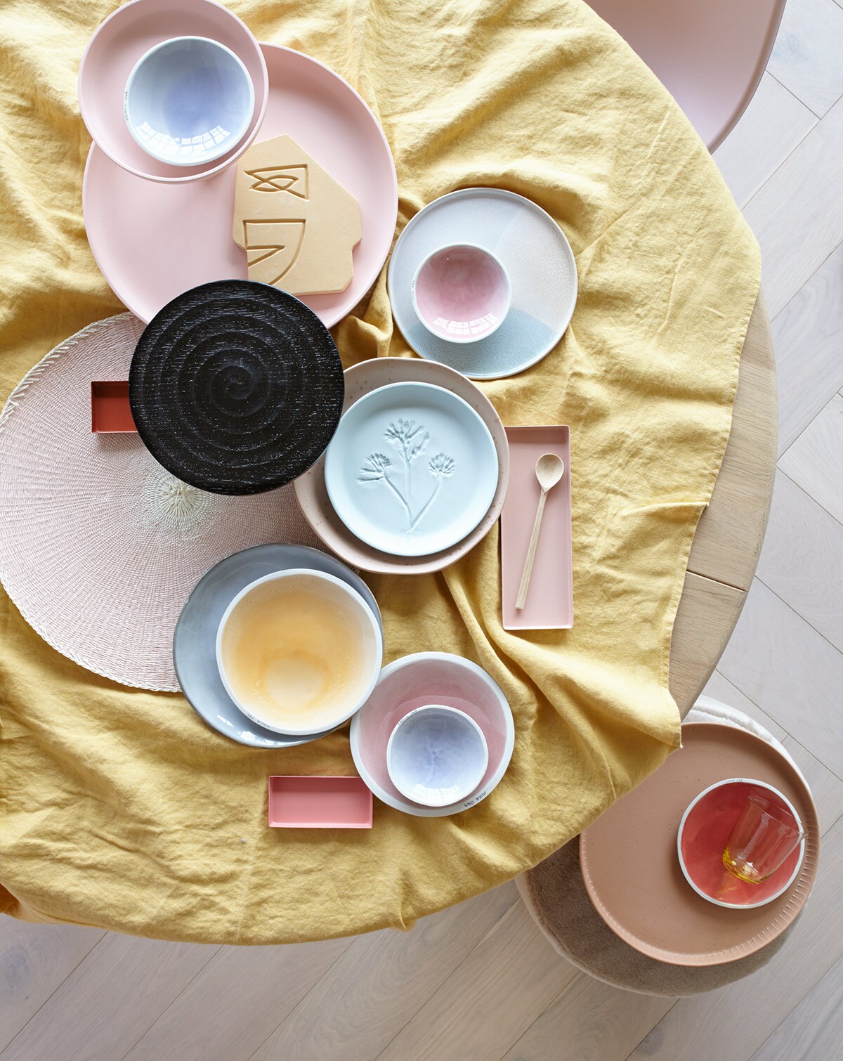 Parket visgraat eiken wit geolied van vtwonen (karwei.nl). Ronde eikenhouten eettafel, roze eetkamerstoel (coosdewitwonen.nl). Geel linnen tafelkleed (letoile.store). Roze etagère (loods5.nl/design). Schaaltjes XS in blauw en roze, S in blauw, M in geel, roze en rood (studioharmenelke.nl). Ornament gezicht, rond bord met opstaande rand, rond terra dienblad (hkliving.nl). Zwarte houten etagère (paviljoennoord.com). Roze placemat (klevering.nl). Niet perfect rond bord met spikkeltjes, vergrijsd blauw bord (loods5.nl). Lichtblauw bord van keramiek met bloemprint (letoile.store). Rechthoekige schaaltjes in verschillende tinten roze, geel glas (hm.com). Houten lepel (restored.nl). Roze fluwelen poef (covanderhorst.nl).