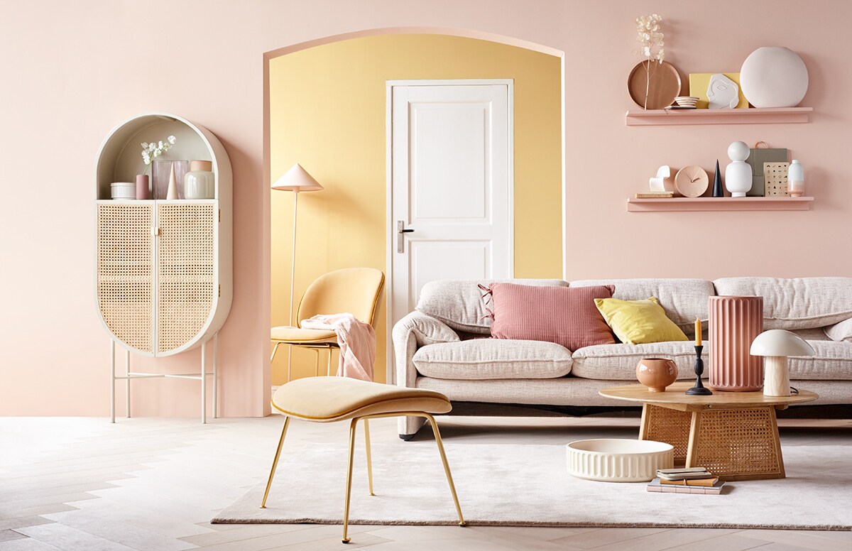 Verf op de voorste wand Vla, achterwand Mosterd van HistorOne (deruverfenbehang.nl). Parket visgraat eiken wit geolied van vtwonen, breedte plank 15 cm (karwei.nl). Kast, roze vloerlamp, roze plaid, salontafel, wit ornament hoofd (hkliving.nl). Voorraadpot van keramiek met deksel, donkerroze vaasje, blank houten kegel, roze kussen met strikjes, zwarte houten kegel (loods5.nl). Zachtroze glazen vaas in organische vorm, miniatuur Vitra designstoel, vaas met bol, spiegel in zachtroze platte ronde vaas (loods5.nl/design). Beige vaas met roze hals, tafellamp met houten poot (coosdewitwonen.nl). Zachtgele fluwelen fauteuil met voetenbank, witte xl schaal van keramiek, roze xl vaas van kveramiek (mobilia.nl). Bank (dekasstoor.nl). Geel fluwelen kussen (hm.com). Vloerkleed in Nougat Rose (vloerkledenwinkel.nl). Roze bolvaas, terra dienblad, gele snijplank (vtwonen.be). Zwarte metalen kandelaar (paviljoennoord.com). Notitieboeken, grijze leren portemonnee, witte kom met roze strepen (klevering.nl). Klok van keramiek, schriften, wit vaasje met roze onderkant (letoile.store). Overig privébezit.