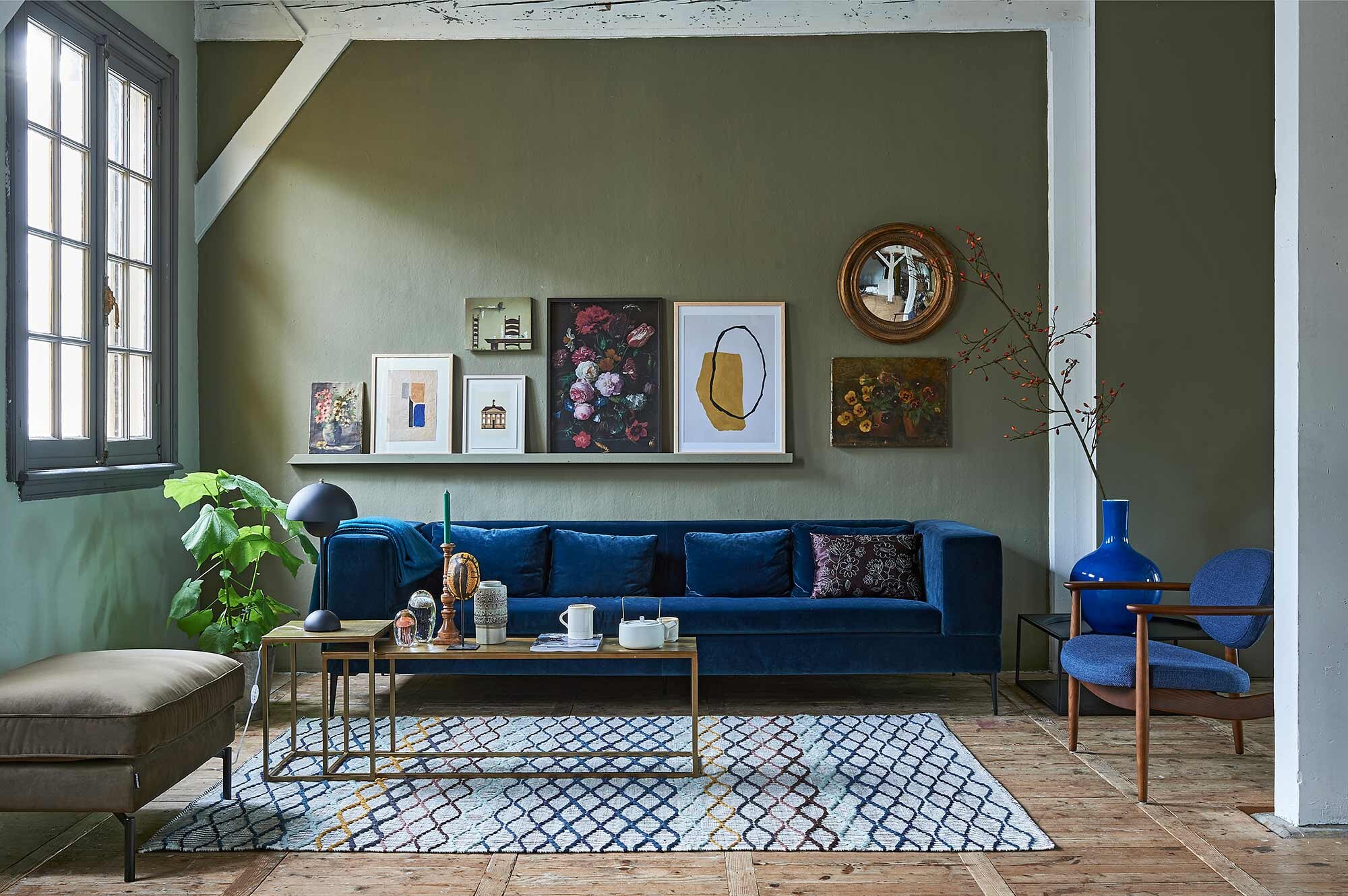 Op de wand muurverf Classico in kleur Tundra (). Bank van blauw velvet, lampje op salontafel (). Salontafel brass, stoel met houten frame, grote blauwe vaas, poef, geborduurd kussen op de bank (). Zwarte metalen bijzettafel, retro vaas, glazen kwallen, namaak schildpad, theepot (hkliving.nl). Kom, kan, rozenbotteltak XL (). Vloerkleed (). Op de wandlijst: v.l.n.r. schilderij met bloemen (privébezit), grafisch werk (), illustratie gemeentehuis van Michiel van der Zanden (), erboven stoel + tafel (privébezit), print bloemen van het Rijksmuseum (), in lijst Hovsta (), grafisch werk (), bloemenschilderij (privébezit). Goudkleurige oude spiegel ().