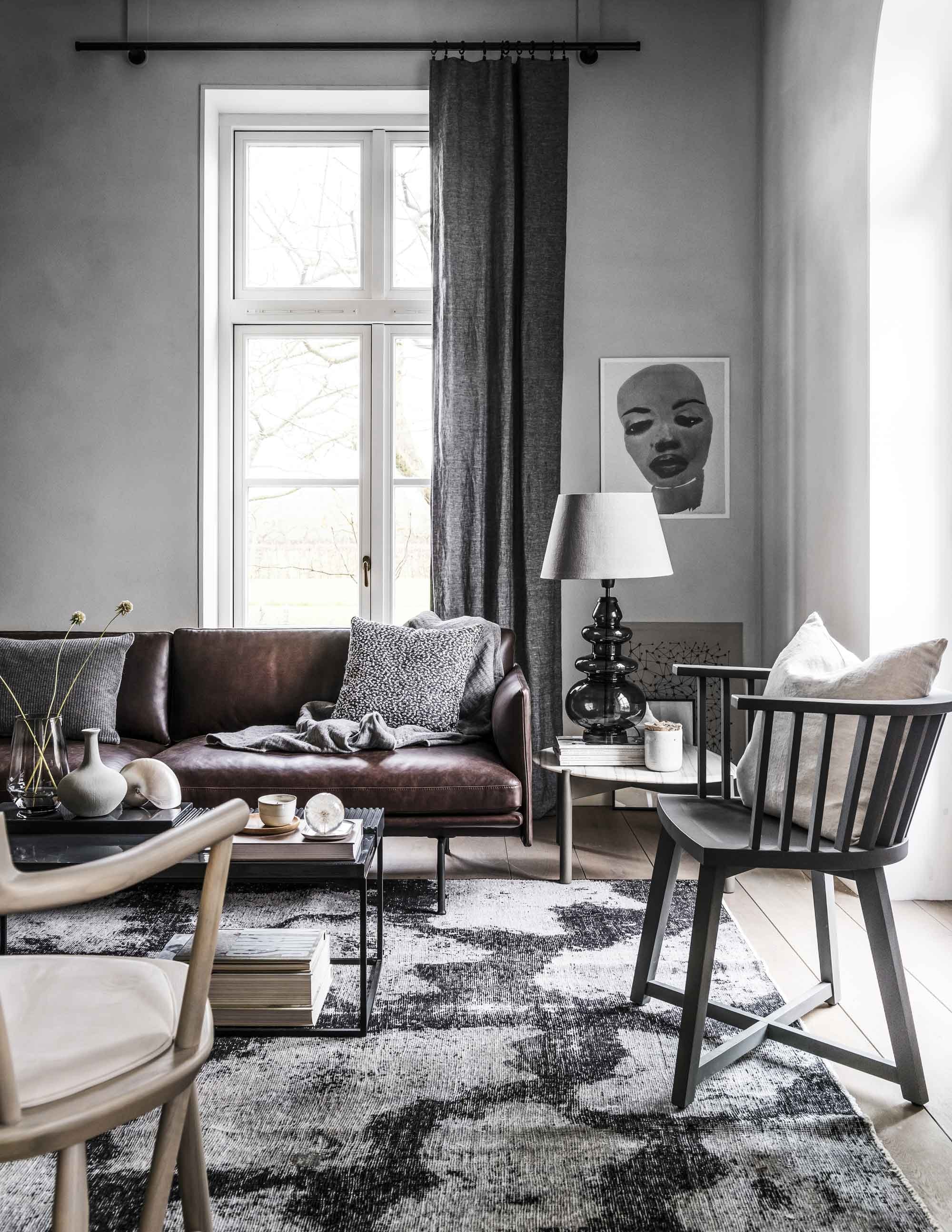 Vloerkleed . Bruine leren bank, grijs kussen, zwart-wit gevlekt kussen . Grijze plaid in wolmix. Linnen gordijn kleur Charcoal, linnen kussen kleur Almond . Poster geprint op grijs karton . Grijze glazen lamp, linnen lampenkap . Marmeren bijzettafel Heath, donkergrijze bijzettafel Terrace met stalen onderstel, vergrijsde houten stoel Oiseau . Donkergijze houten spijlenstoel . Grijze glazen vaas uit een set van 3 . Grijs vaasje van keramiek . Schelp . Houten bord, lichtgrijze porseleinen kom met soy wax . Overig privébezit.