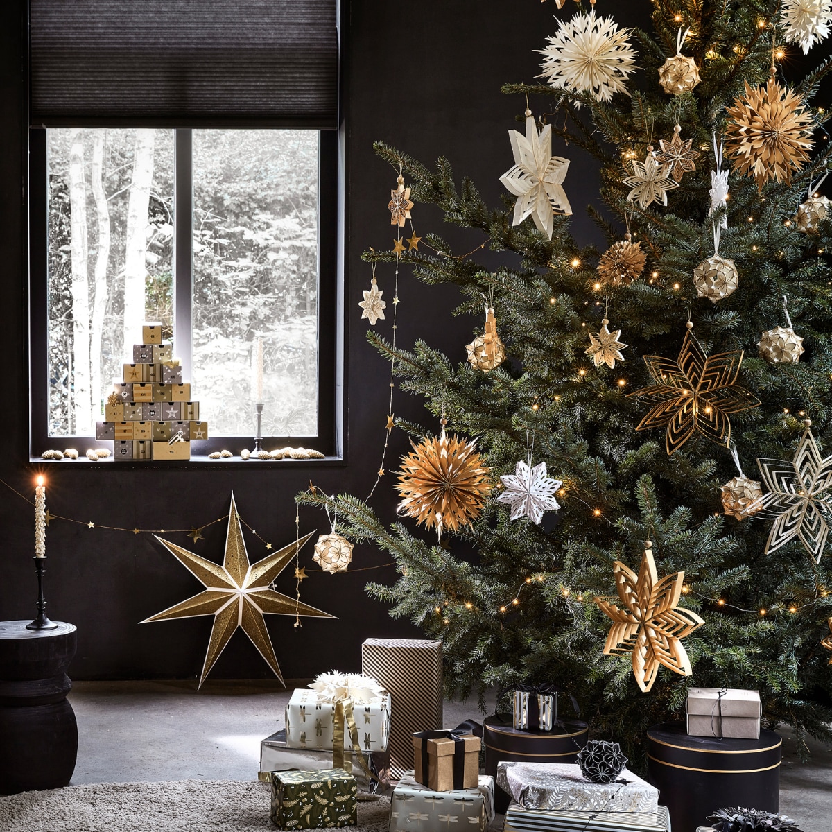 Kartonnen adventskalender € 27,99, goudkleurige kaars met glitter, per 2 € 6,99, goudkleurige papieren ster, 70×19 cm (Øxd) € 9,99, goudkleurige metalen slinger met sterren, 210 cm (l) € 3,49 (ook verkrijgbaar in zilver). In de boom: diverse papieren ornamenten in de kleuren goud, wit, zilver en zwart, per stuk vanaf € 2,49, zilverkleurige lichtslinger warm wit met 30 ledlampjes op batterijen inclusief display en timer, 300 cm (l) € 3,99. vtwonen 12-2022 | productie Tanja Saarberg, Isa Hoevens | styling Kim van Rossenberg | fotografie Peggy Janssen
