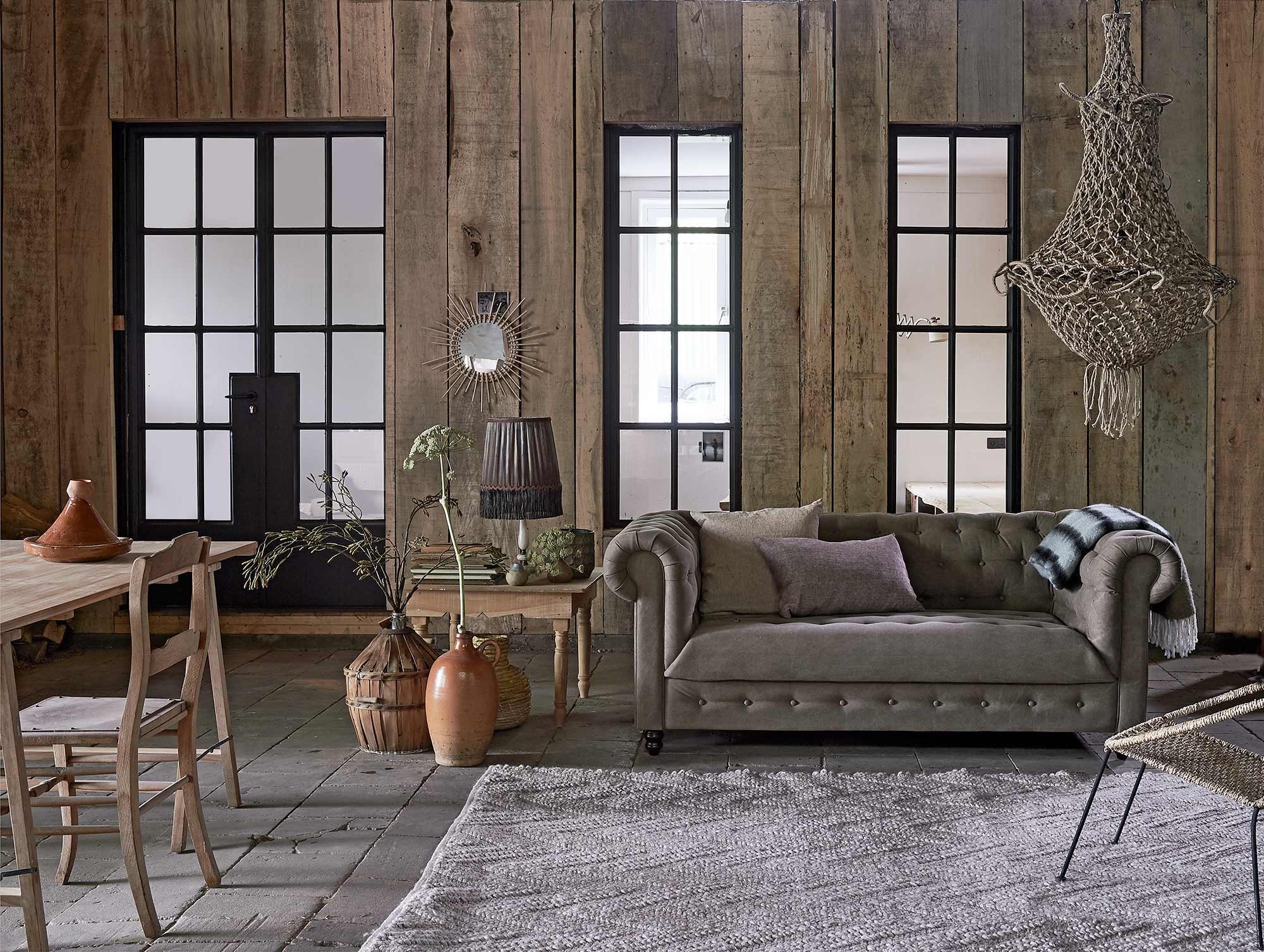 Bank Chester (Dutchbone). Kussen van By Mölle (Nijhof). Karpet Punja (Zuiver). Houten salontafel (Household Hardware).Vintage schemerlamp (MaisonNL). Donkere vaas met cirkeldessin, vaasje met blauwe rand, kunsttak in gistfles, schragentafel (HKliving). Stenen kruik, gistfles met riet, houten stoel (Burbri Antiek). Rotan vaas (IKEA). Tajine, rotan spiegel Soleil (Household Hardware).
