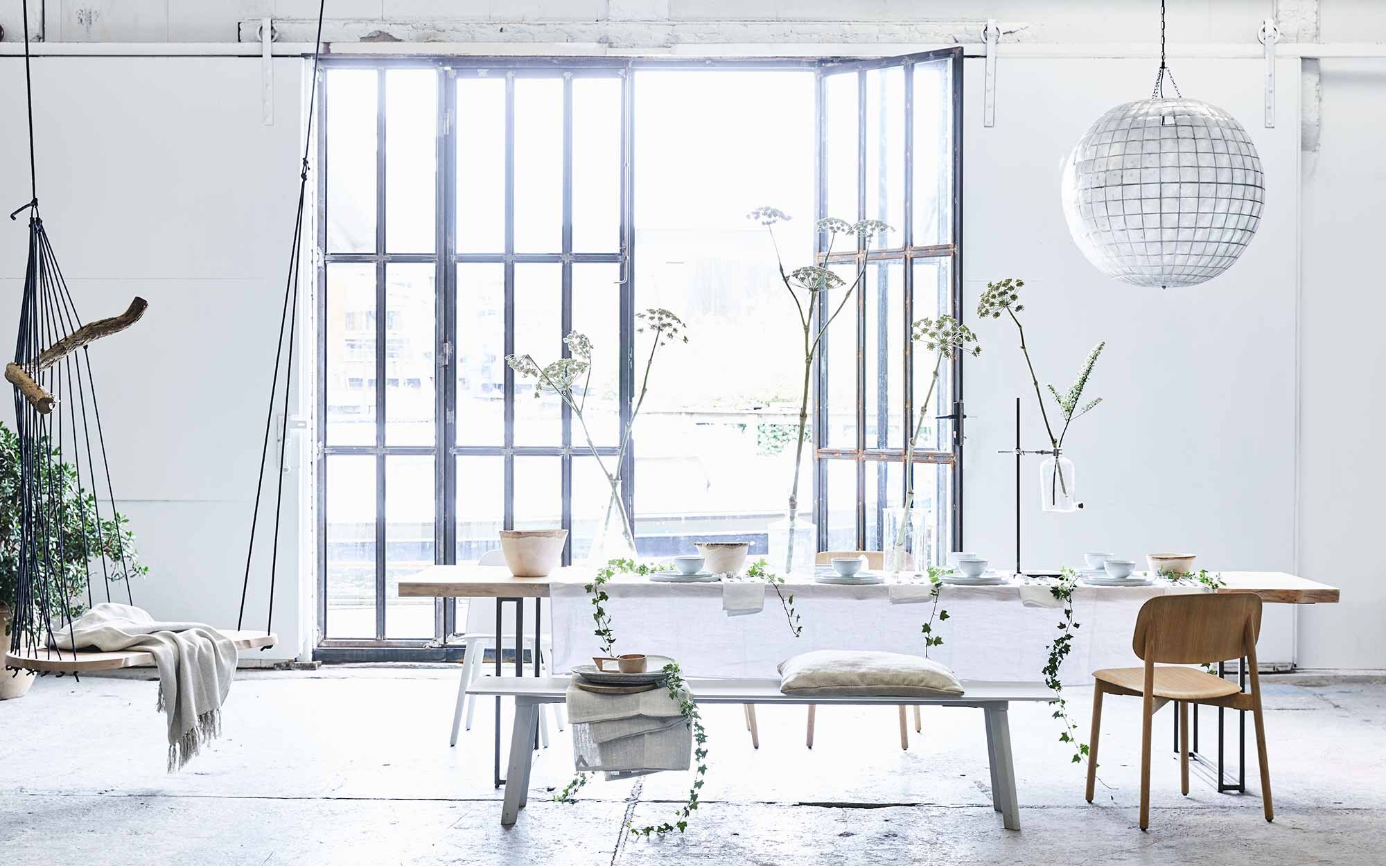 Tafelkleed in optic white, servetten, hoge houten schaal, houten bekers met oor (). XL bollamp van schelpen, grote witte borden, kleine borden, kommen, houten schaal, keramische schaal op bank (). 24-delig bestek Behagfull (). Labflessen divers, lab standaard (). Eettafel Altar van Jesse Sanderson, hangstoel Floating divan van Chiel Kuijl (). Grijze bank Copenhague Deux Bench, houten stoelen Soft Edge (). Witte stoel Nerd van Muuto (). Plaid in stoel, kussen (). Linnen laken op de bank van No.6 (). Overig privébezit.,