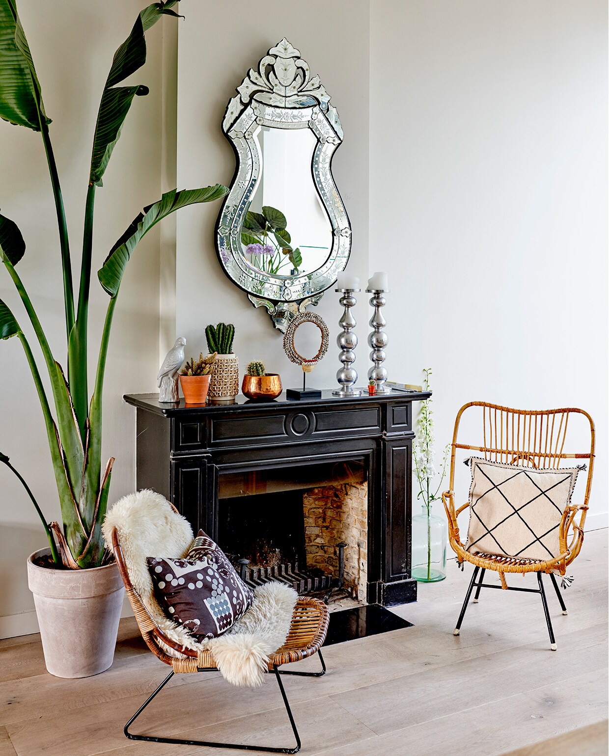 Spiegel uit een curiosawinkel in Amsterdam. Beeld van vogel is een geschenk. Cactussen van Dennis Flowers. Aardewerken pot van Zara Home, koperen pot Atelier 8. Kandelaars Hema. Afrikaanse ketting van schelpjes is een geschenk. In de glazen vintage vaas op de grond van Ivonne Old Furniture Antwerpen werd vroeger arsenicum bewaard. Bloesem- takken Miss Bloem. Hoge rotan jaren 70-stoel van de kringloop. Lage rotanstoel van House Doctor. Kussen van wol met lovertjes is souvenir uit Marokko. Bananenplant van Dennis Flowers.