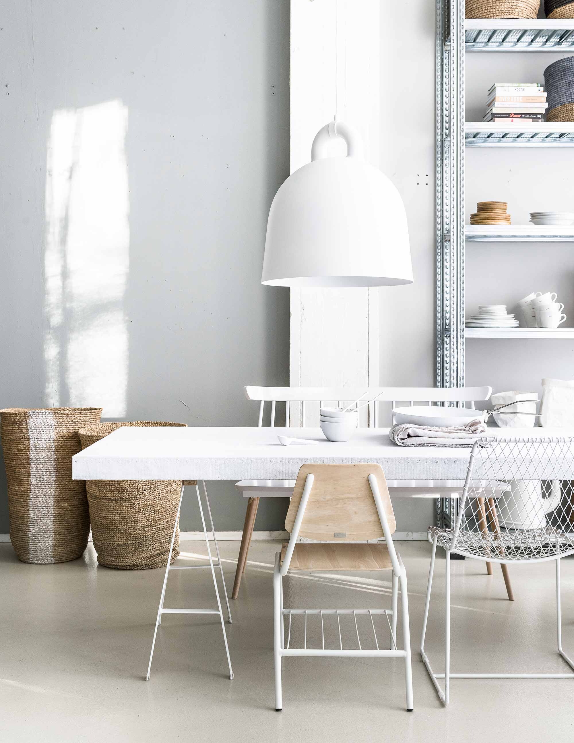 Op de muur krijtverf, lamp Large Bell van Normann Copenhagen, stoel van draadstaal, bankje, rieten manden, kleine mand, houten kommen (Loft). Tafelblad bekleed met doek (Combitex). Schragen, stoel met houten zitting van Studio Simple (Serax). Servies, papieren opbergzakken en stellingkast A La Carte p.o.a. (Transvorm). Linnen laken (House in Style). Pan en losse klem van KnIndustrie (Do’s). Porseleinen lepels (Serax).