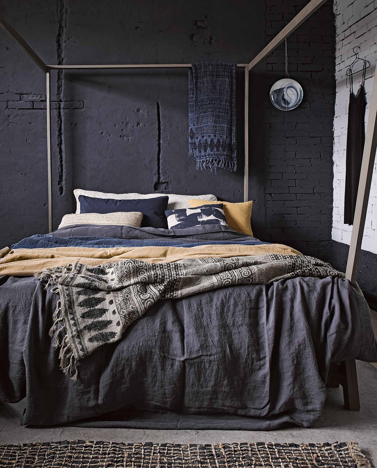 Hemelbed Safari (). Linnen dekbedovertrek in offblack antraciet, kussen met gestempeld motief (). Donkerblauwe doorgestikte sprei, linnen doek met dessin in naturel en inktblauw, vloerkleed van geweven touw met leren stroken, alles van Madam Stoltz (). Specerijengeel linnen laken van Society vanaf, donkerblauwe katoenen kussenhoes van Society (). Kussen van geweven touw (). Kerriegeel linnen kussen ). Broodzak van vlas (). Bord aan de muur (). Jurkje ().