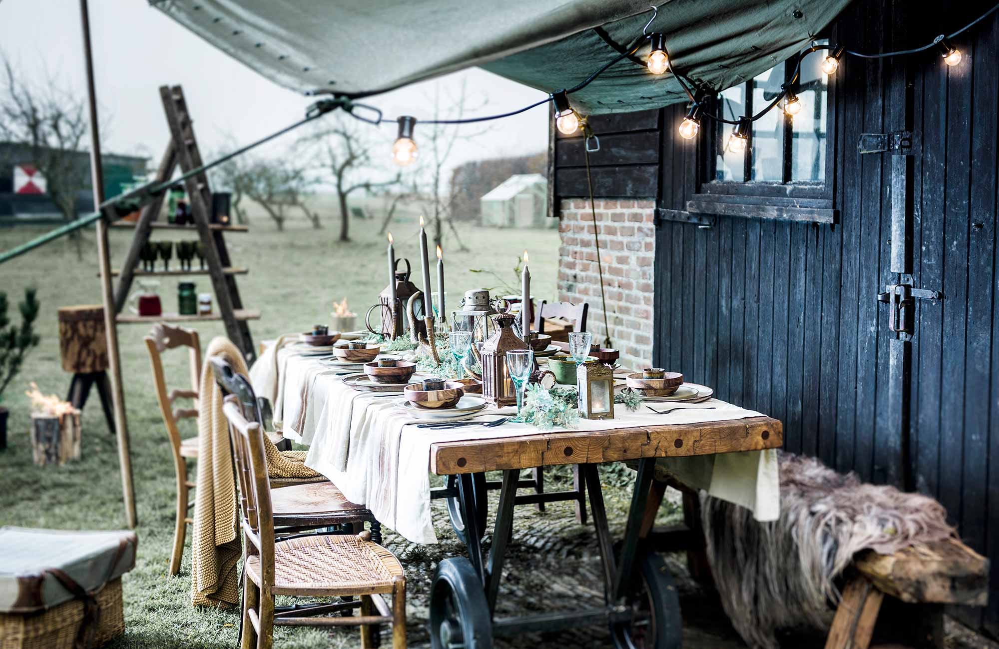 Tafel (). Zetel (). Taupe tafelkleed, okergeel plaid, wijnglazen (). Houten stoelen, groot hakblok (). Rieten mand met groene klep, ladder (). Groen legerdoek (). Bruine schapenvacht, kaarsen (). Lantaarns, grote gouden kaarsenstandaard (). Espressokopjes, houten kommetjes van HK Living, groene borden van Serax, grote wit-bruine borden van Bloomingville, vuurfakkel (). Wit bord met gouden randje (). Zwart bestek (). Bruine trui, bruine rok ().,
