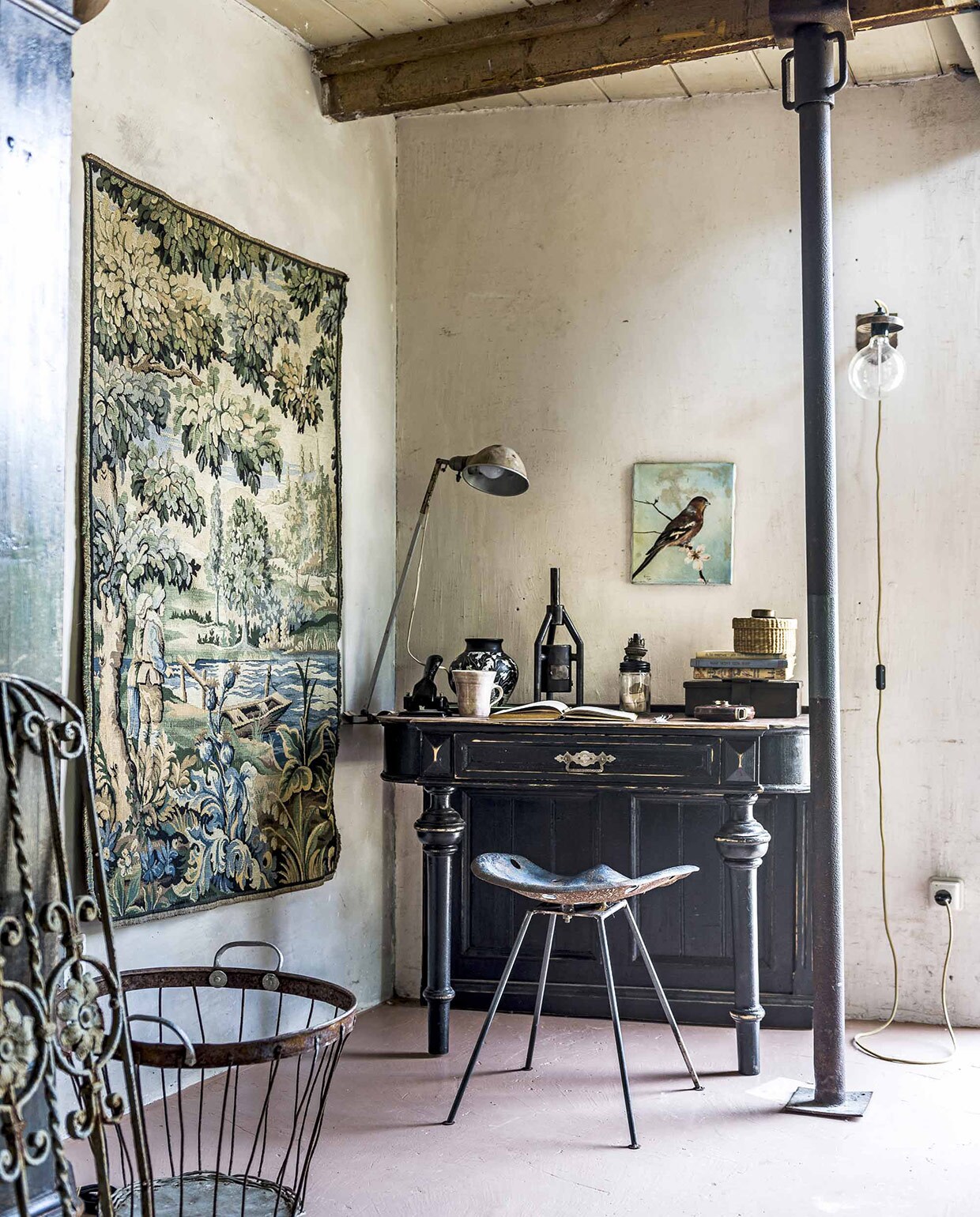 Wandkleed, zwart bureau (). Vintage designkruk, beker (). Bureaulamp, minikacheltje (). Geldkist (). Vaas ). Metalen draadmand (). Kantoorbenodigdheden, rieten mandje op bureau van een kringloopwinkel, overig privébezit.