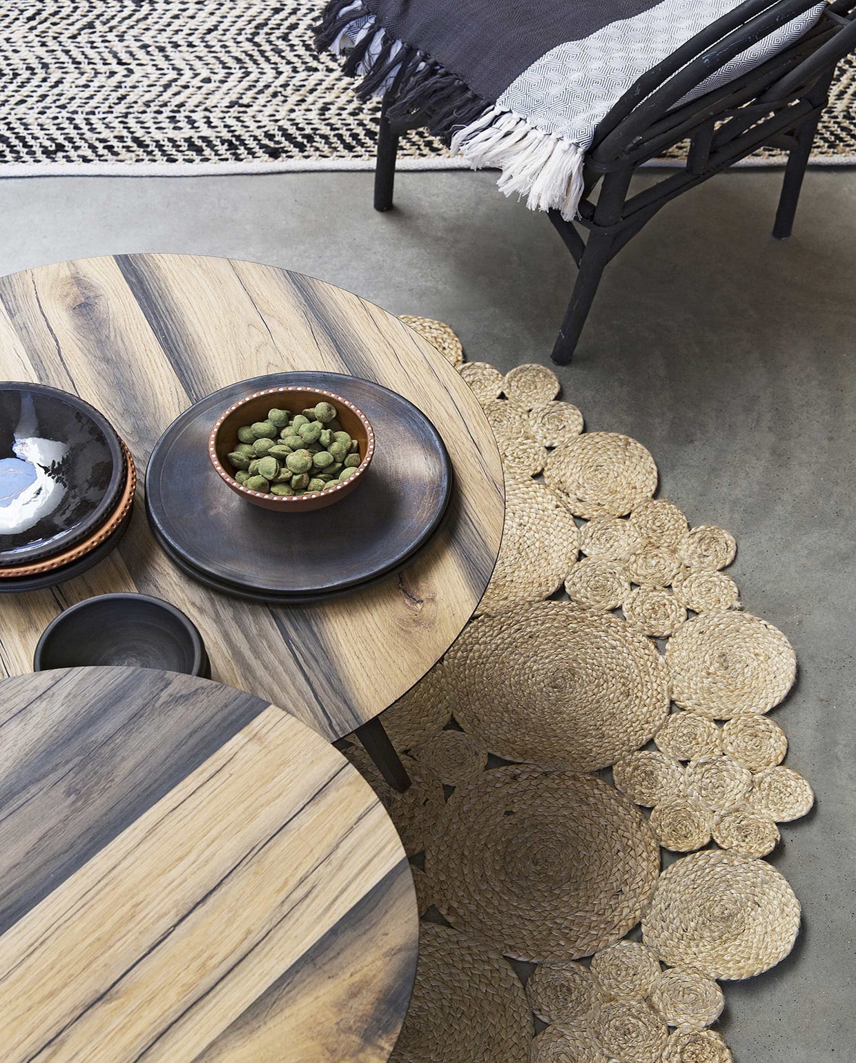 Vloerkleed met zigzagpatroon van leer en katoen, vloerkleed Mandala Carpets (Zenza Home). Eiken salontafel Slo Savon (Design 020). Zwarte rotan stoel (Household Hardware). Plaid (Raw Materials). Aardewerk van Beate Snuka vana (The Frozen Fountain).