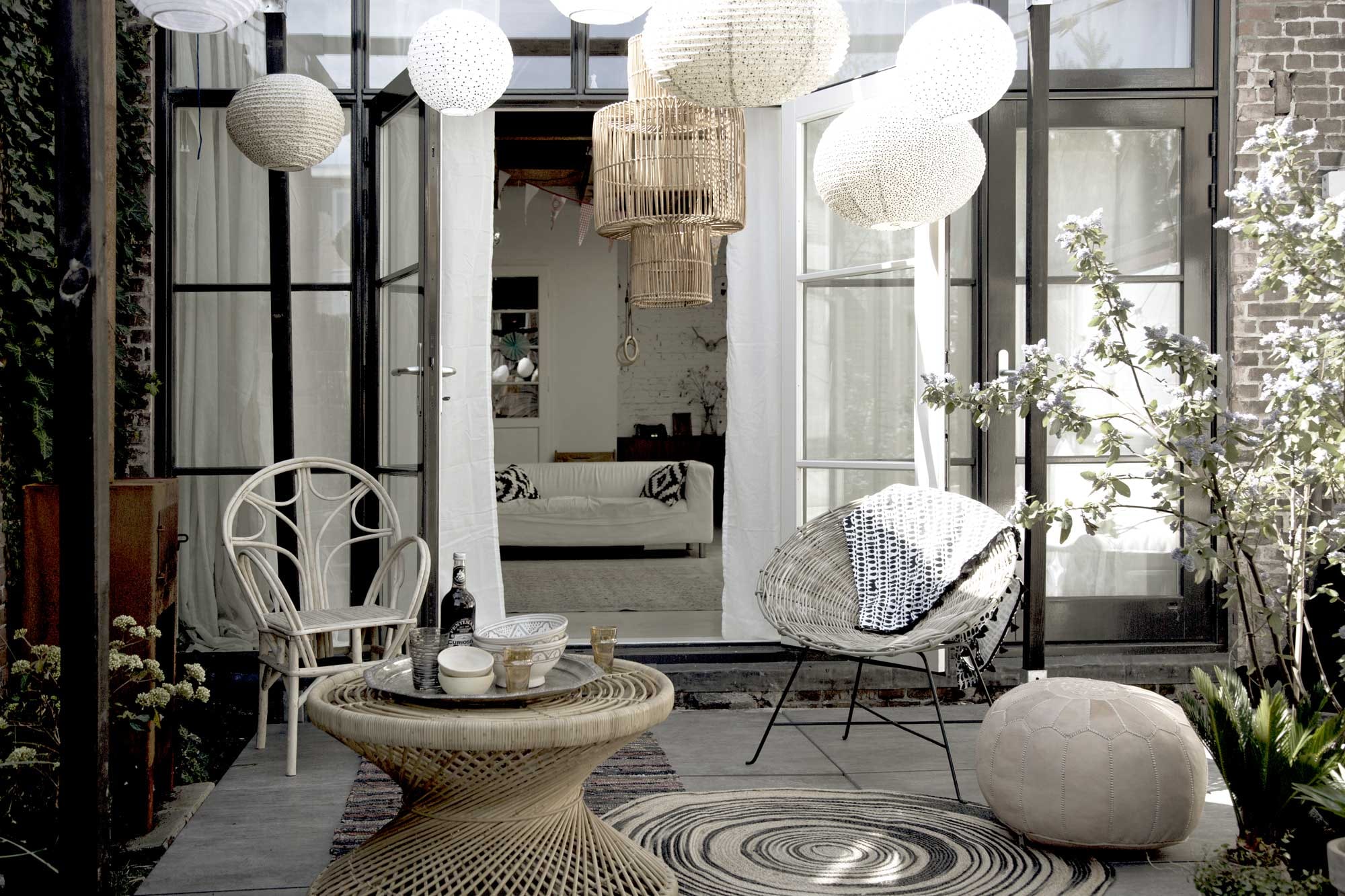 Pergola, Cubic Pergola Systeem (). Lampion large met zwart-witte stip, lampion medium met graniet/zwart/wit, lampion medium wit met gouden stip, lampion medium met roze-gouden stip (). Rotan lamp, rotan tafel, ronde potten, hoge potten (). Stoel links, houten schaaltjes, oranje glazen, keramische kommen in grijs-wit, poef (). ,  (HK Living). Dienblad in zilver (). Rotan stoel rechts(). over stoel (H&amp;M).  (Storebror). Tegels Solostone Beachwood Antracite van vtwonen (). Overig privébezit.