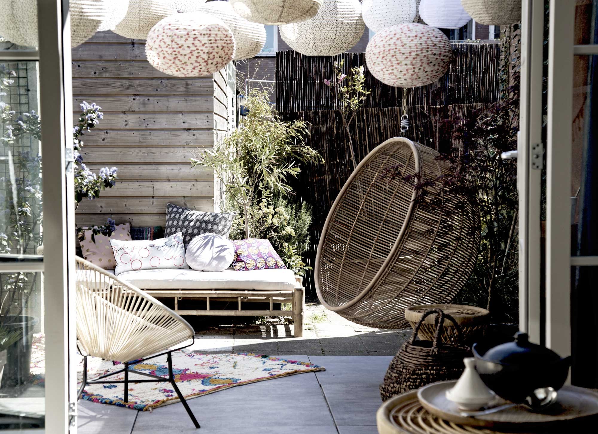 Pergola Cubic Pergola Systeem (). Lampion in graniet/zwart/wit, lampion met zwart-witte stippen (). Bamboe schutting ().  (HK Living). Roze kussen met gouden stip, rond kussen (). Kussen met gekleurde print (). Grijs kussen met witte stip, kussen met roze cirkels, rotan mand, tegels Solostone Beachwood Antracite van vtwonen, houten bord van HK Living (). Kussen in roze en geel, soeplepel, tajine (). Bamboe ligbed inclusief kussen, Tine K Home (). Touwstoel van Bodilson (). Kleed (). Rotan tafel klein, rotan tafel groot ().  (Raw Materials). Witte lampion privébezit.