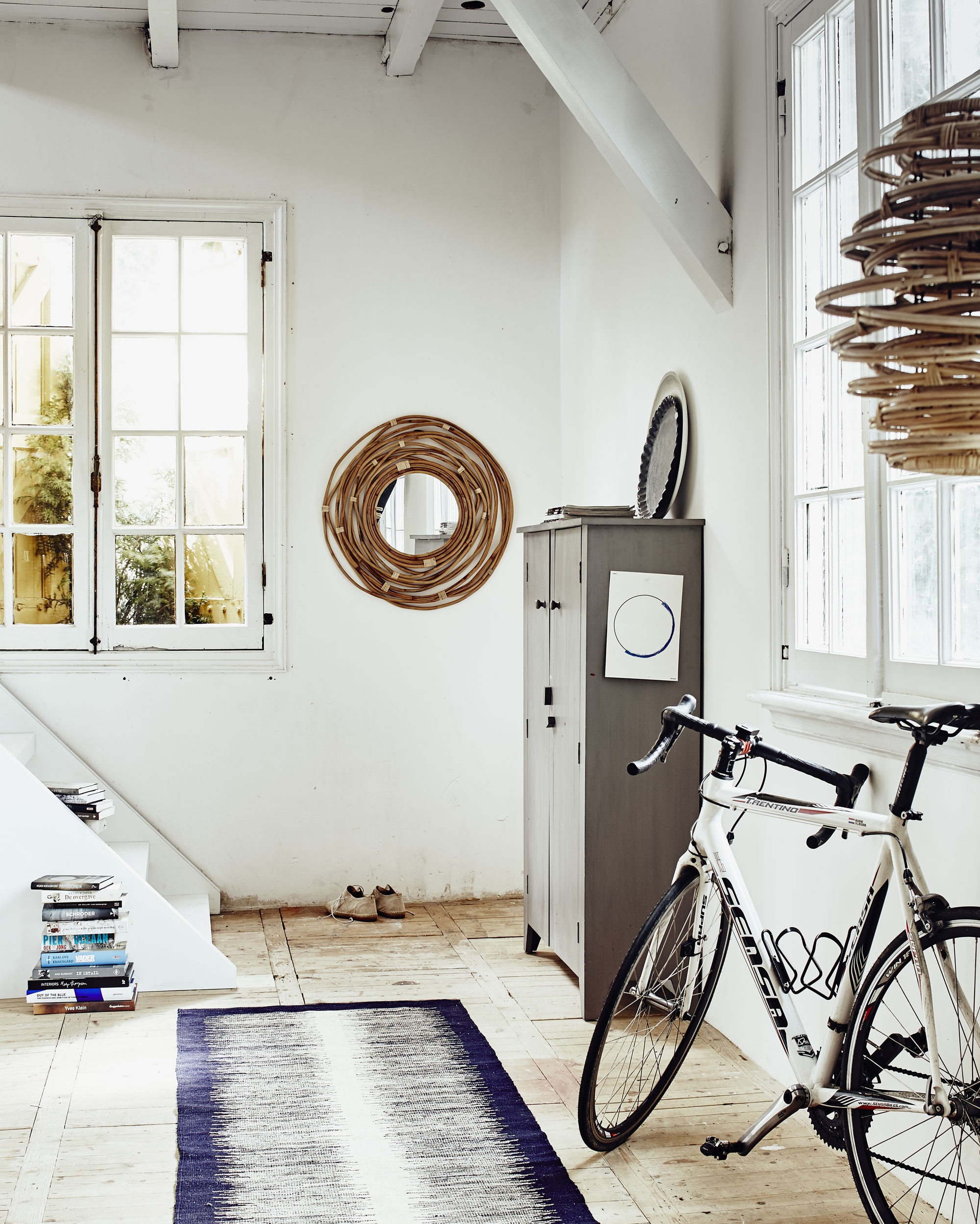 Kast (). Houten bord, grijs aluminium bord (). Spiegel Kubu, gevlochten hanglamp (). Wollen vloerkleed (). Linnen schoenen van Humanoid (). Kussenovertrek Fjälljung (). Fiets privébezit.