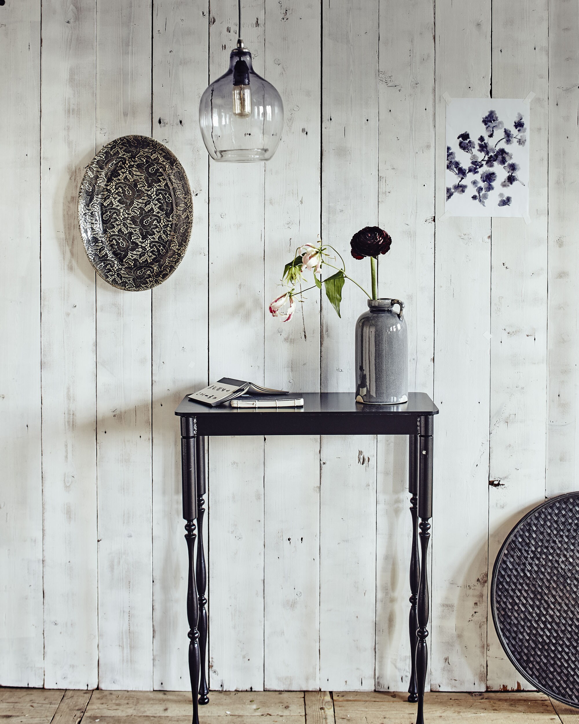 Stalen tafeltje, ovalen bord met kantprint aan de wand (). Glazen hanglamp (). Dienblad (). Aardewerken kan met oor (). Notitieboekjes ().