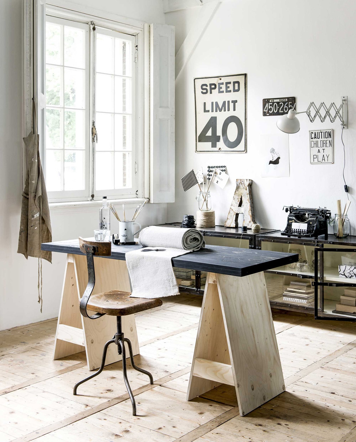 Metalen bord Speed Limit, nummerbord, oude metalen letter A (Spoor 38). Print op de muur Kim by Dufay Alice (L’Affiche Moderne). Wandlamp Aberdeen van It’s About RoMi, zwart-witte opbergdoos Remember (vtwonen.nl). Voorraadpot met deksel Korken, schriften, tapehouder met tape Fullfölja (Ikea). Stoffen vlaggen Hurray Flags (Ferm Living). Metalen dressoir Vegas van New Routz (Het Kabinet). Atelierkruk Pleven (Brût Amsterdam). Overig privébezit.